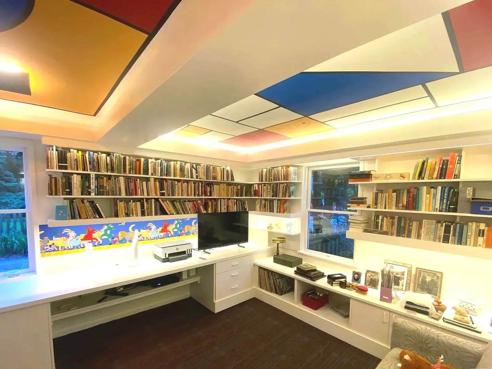 White wraparound library desk and shelves under a color-block ceiling