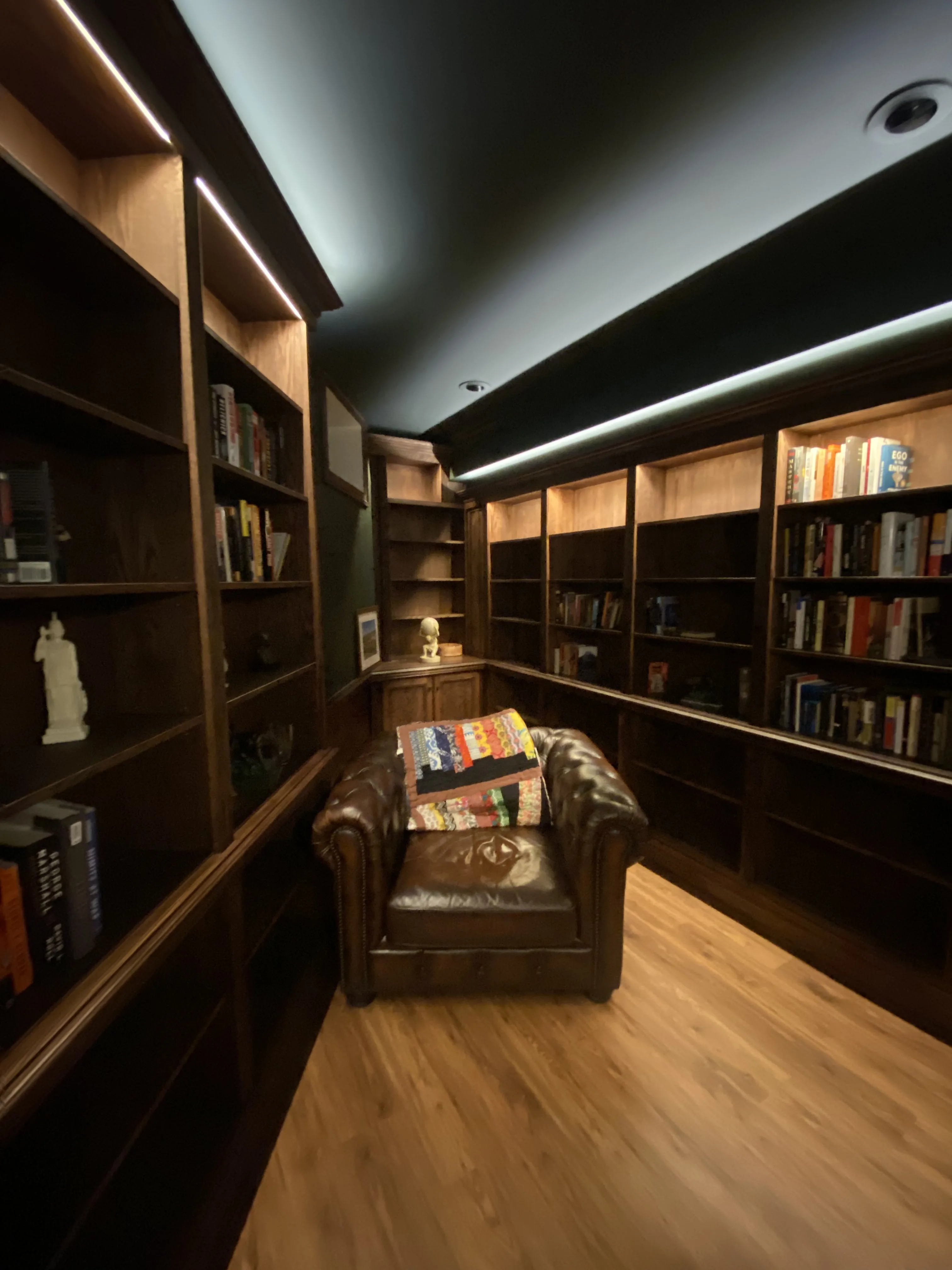 Finished custom stained-oak built-in library/study: floor-to-ceiling bookcases, base cabinets, reeded stiles, LED cove lighting