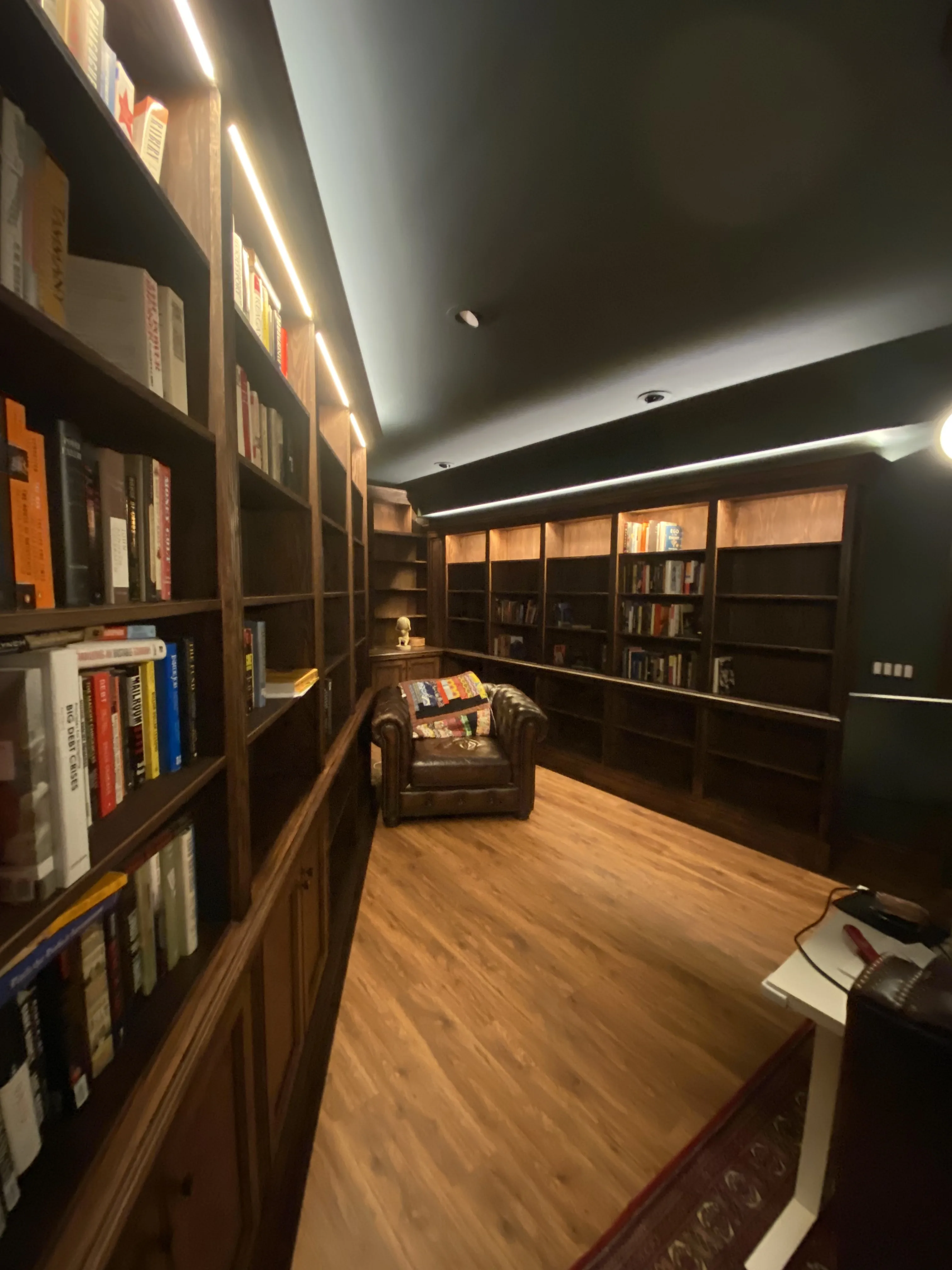 Finished custom stained-oak built-in library/study: floor-to-ceiling bookcases, base cabinets, reeded stiles, LED cove lighting