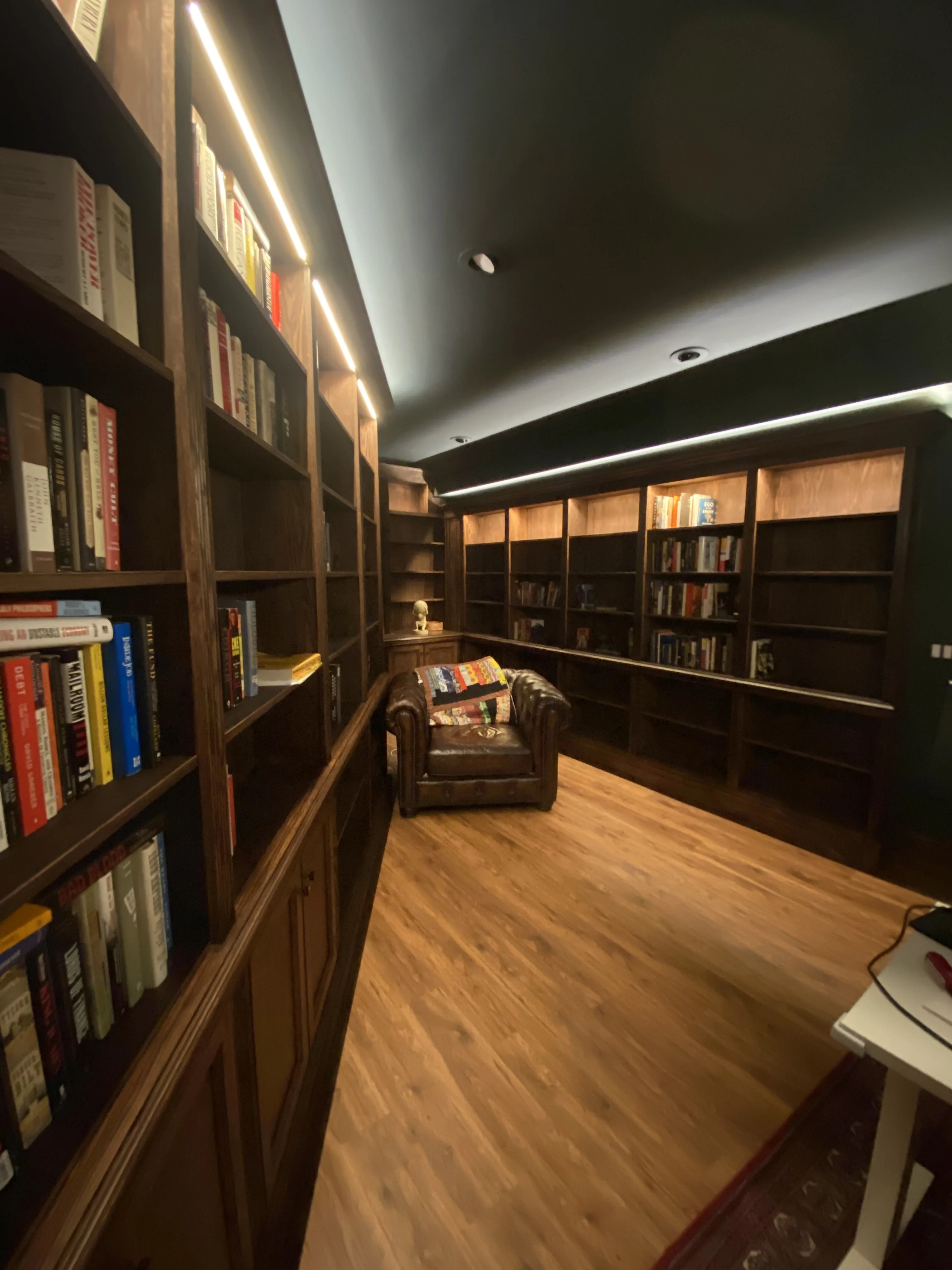 Finished custom stained-oak built-in library/study: floor-to-ceiling bookcases, base cabinets, reeded stiles, LED cove lighting