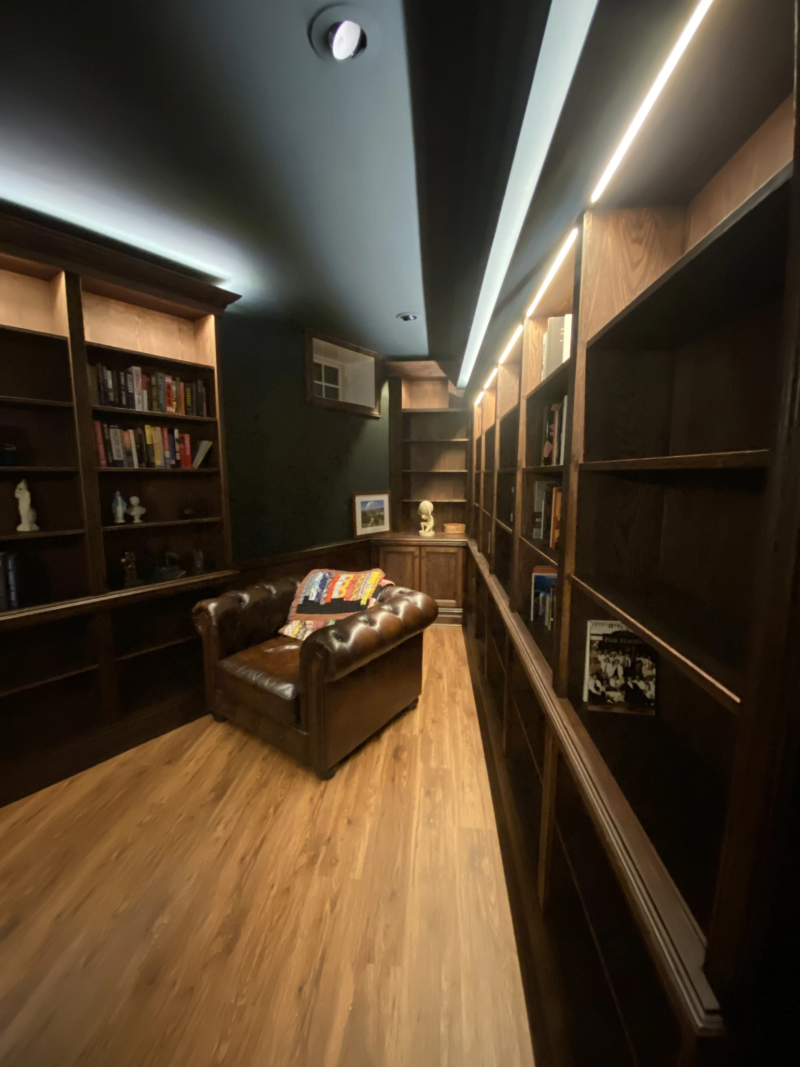 Finished custom stained-oak built-in library/study: floor-to-ceiling bookcases, base cabinets, reeded stiles, LED cove lighting