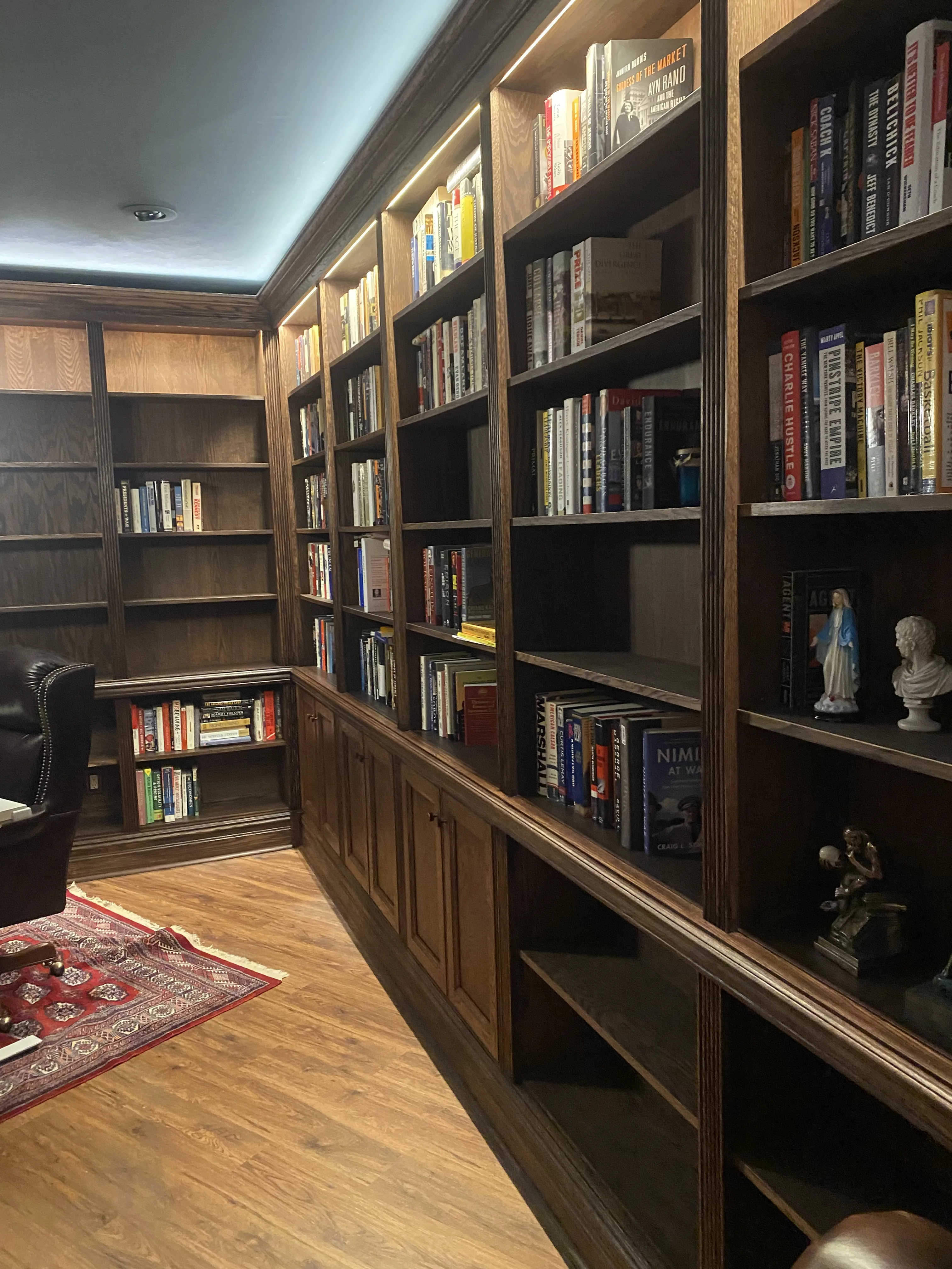 Finished custom stained-oak built-in library/study: floor-to-ceiling bookcases, base cabinets, reeded stiles, LED cove lighting
