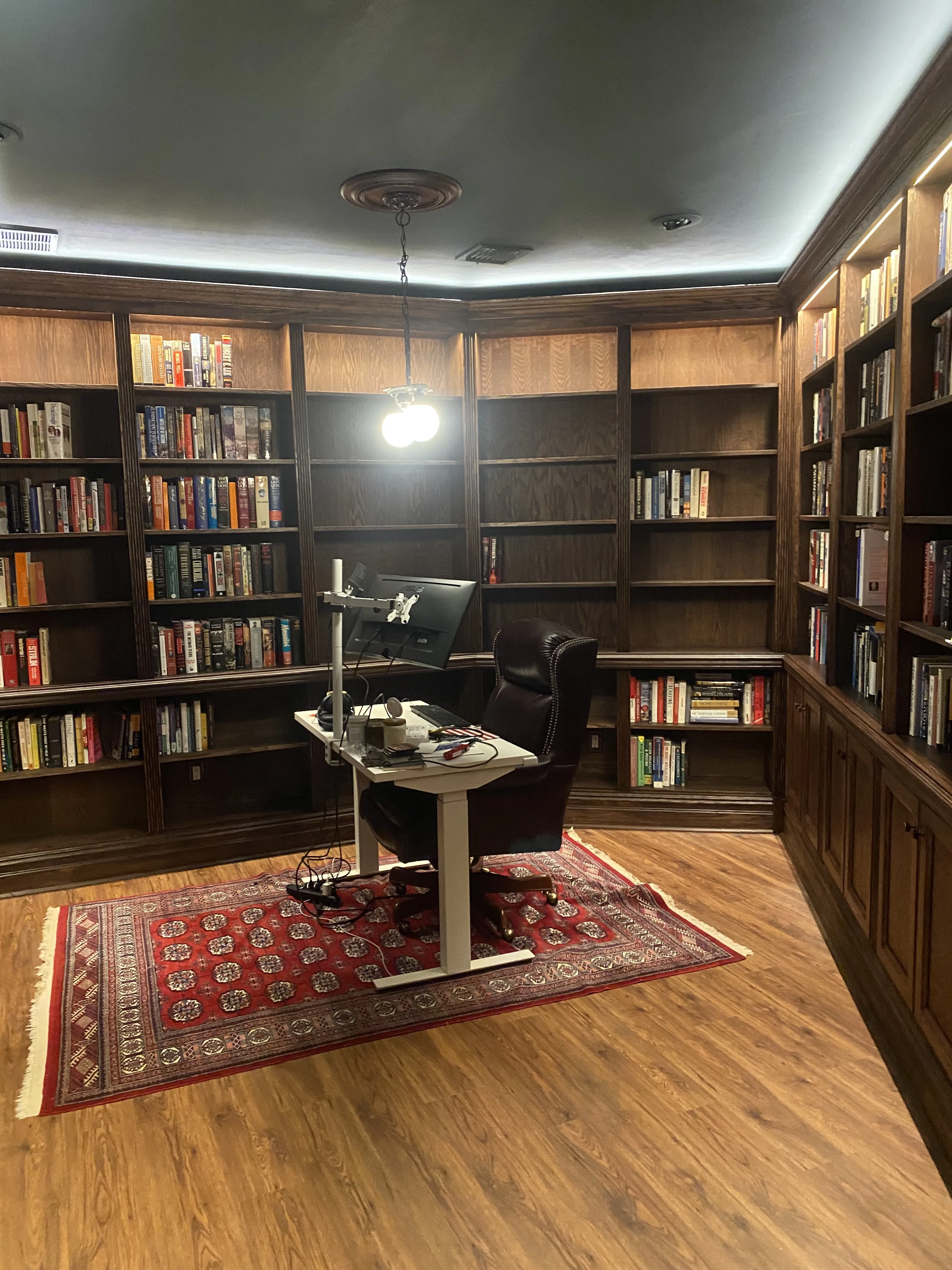 Finished custom stained-oak built-in library/study: floor-to-ceiling bookcases, base cabinets, reeded stiles, LED cove lighting