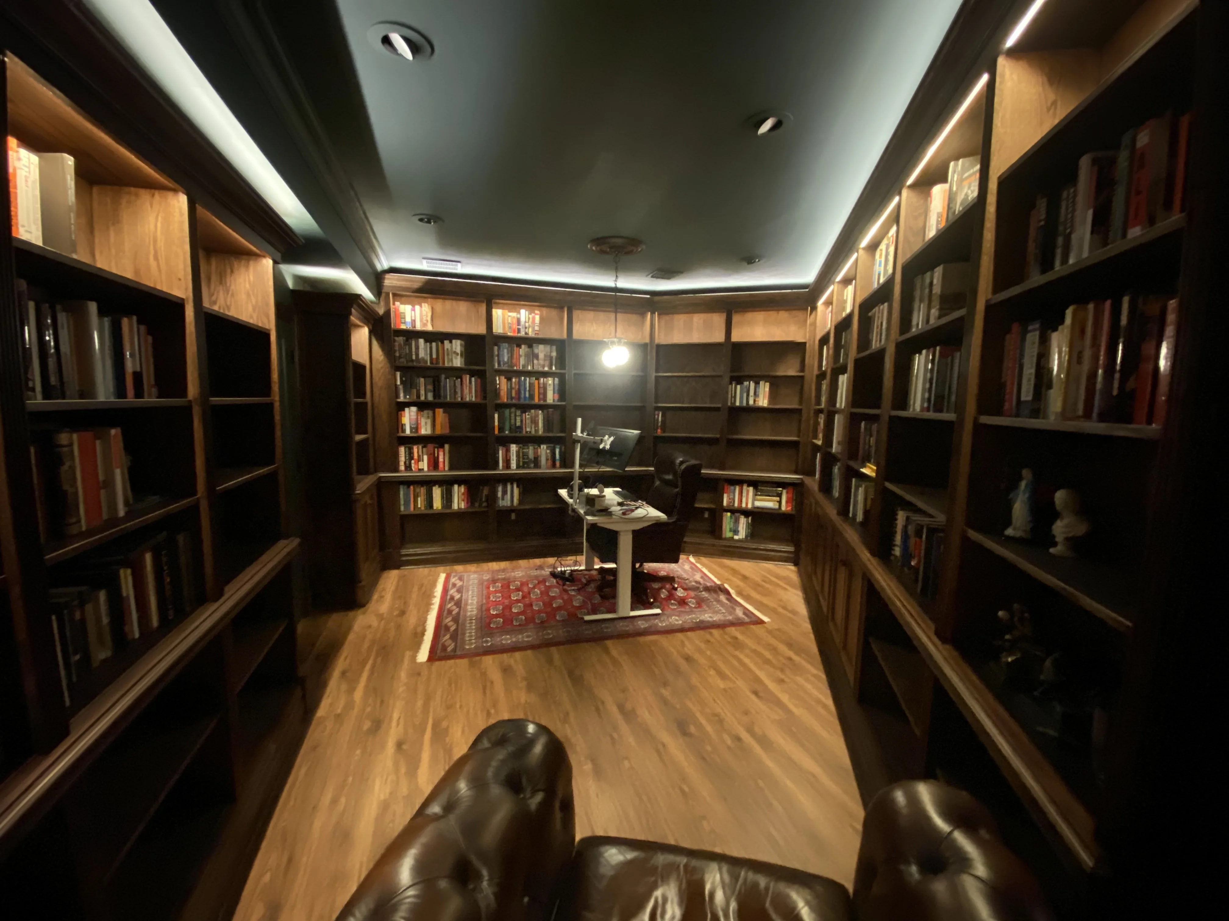 Finished custom stained-oak built-in library/study: floor-to-ceiling bookcases, base cabinets, reeded stiles, LED cove lighting