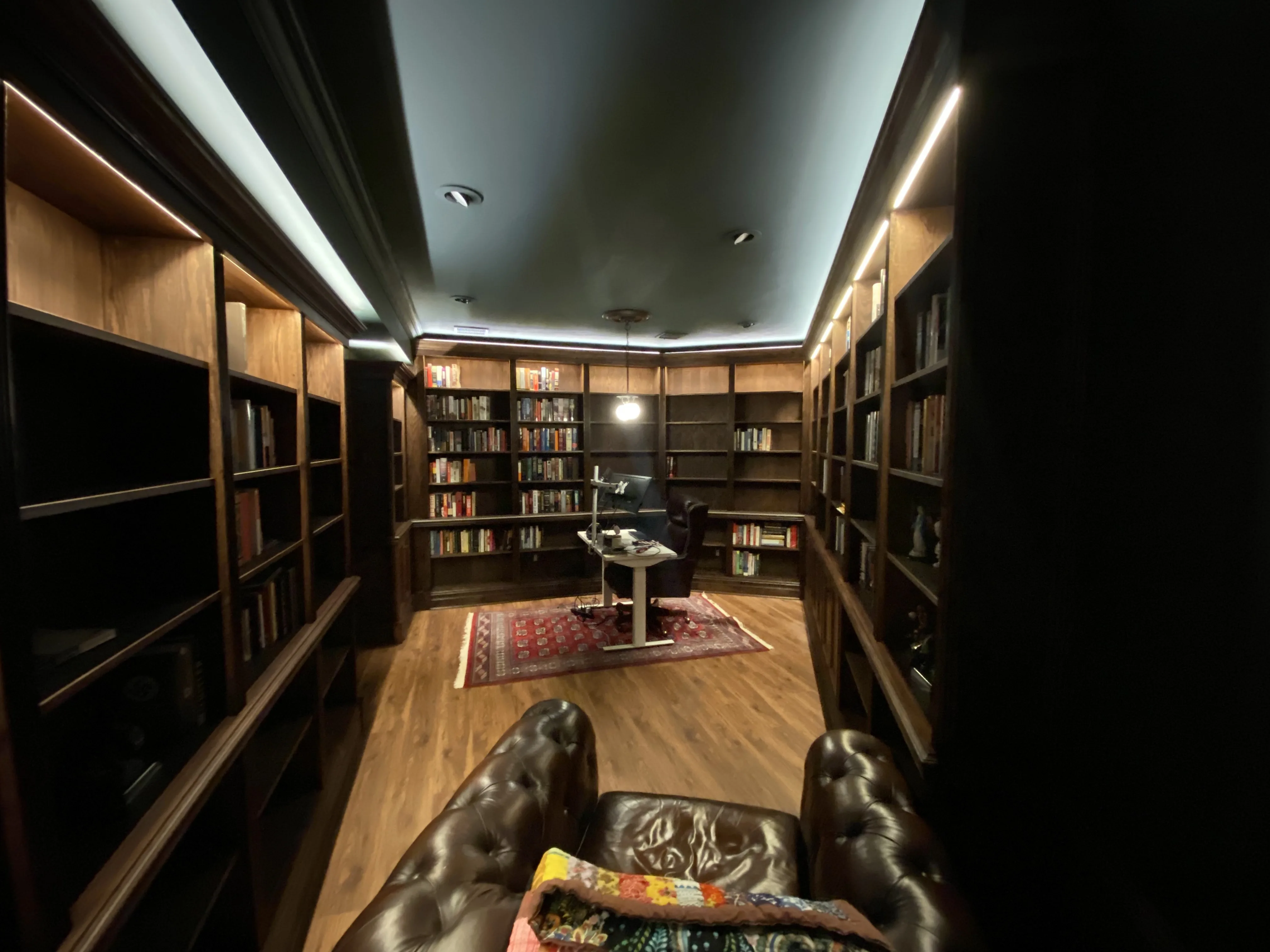 Finished custom stained-oak built-in library/study: floor-to-ceiling bookcases, base cabinets, reeded stiles, LED cove lighting