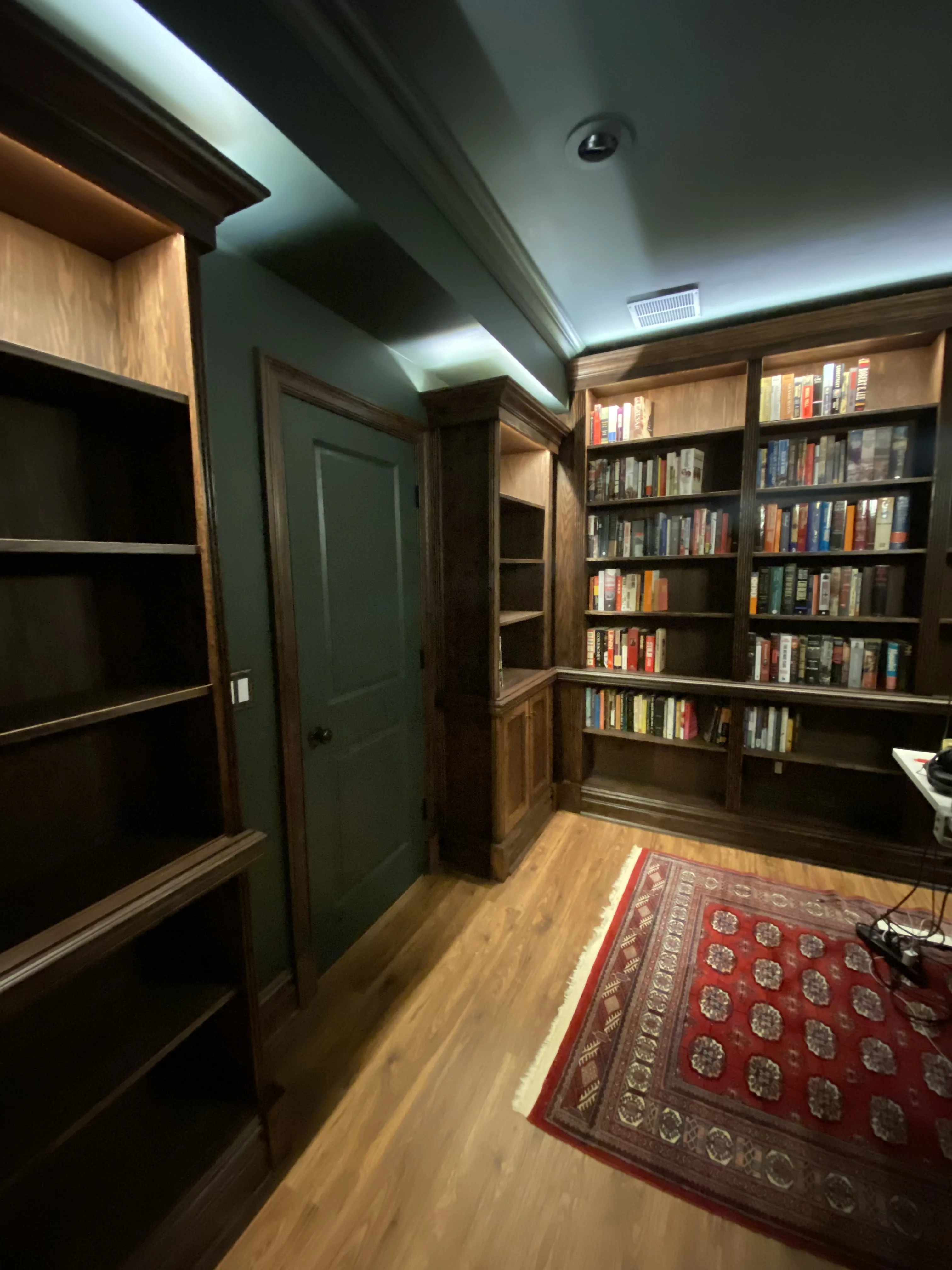 Finished custom stained-oak built-in library/study: floor-to-ceiling bookcases, base cabinets, reeded stiles, LED cove lighting