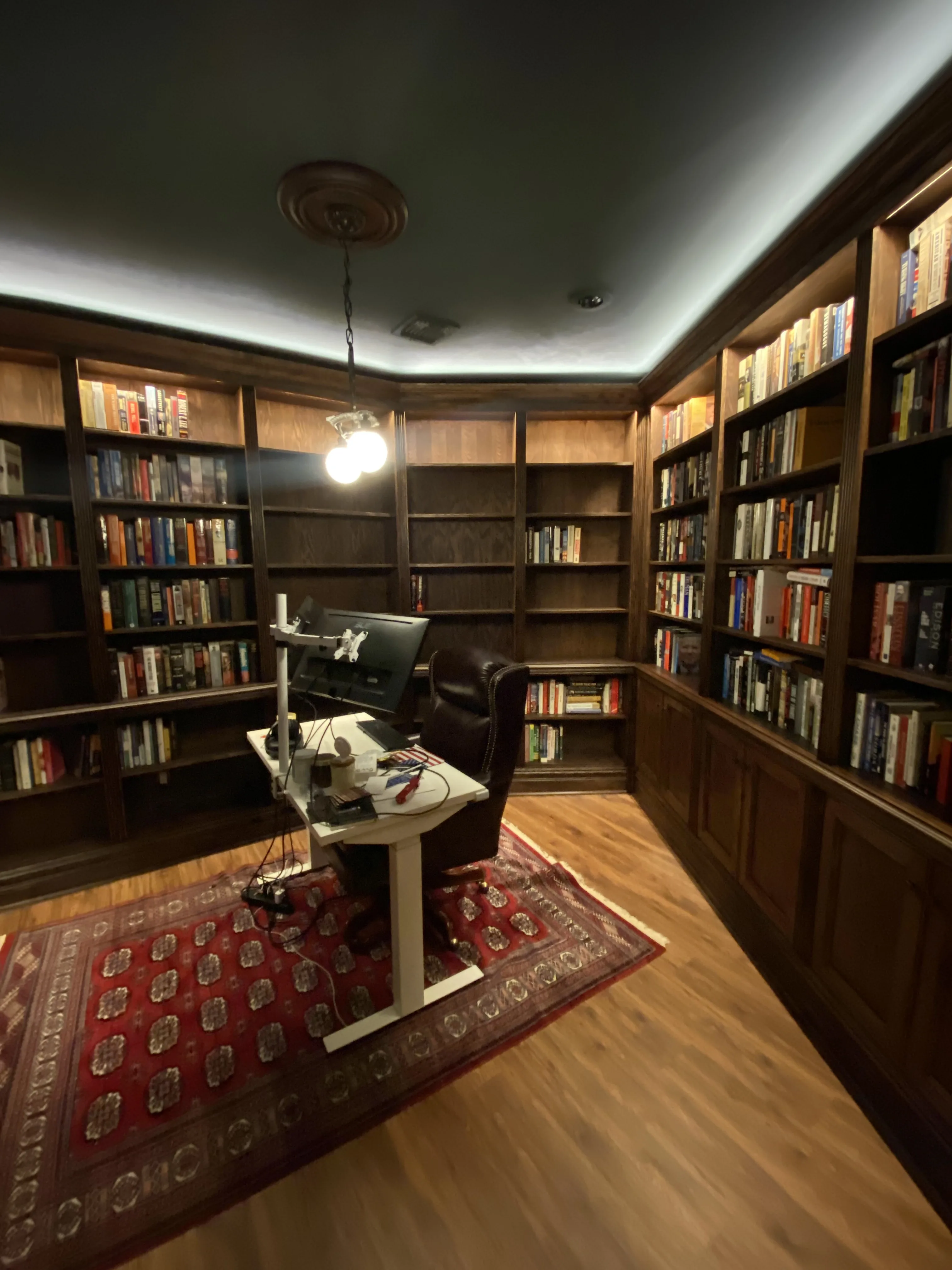 Finished custom stained-oak built-in library/study: floor-to-ceiling bookcases, base cabinets, reeded stiles, LED cove lighting