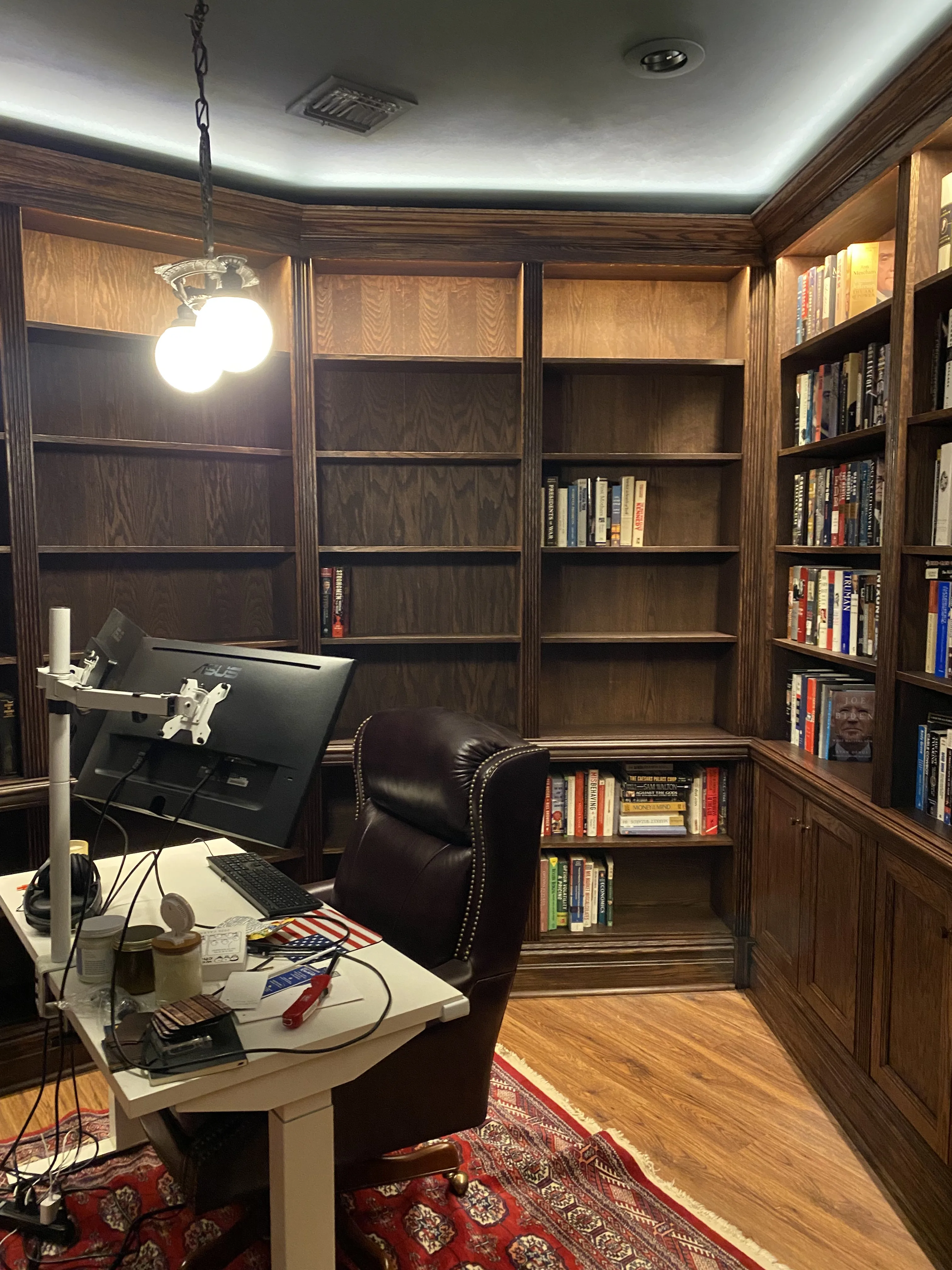 Finished custom stained-oak built-in library/study: floor-to-ceiling bookcases, base cabinets, reeded stiles, LED cove lighting