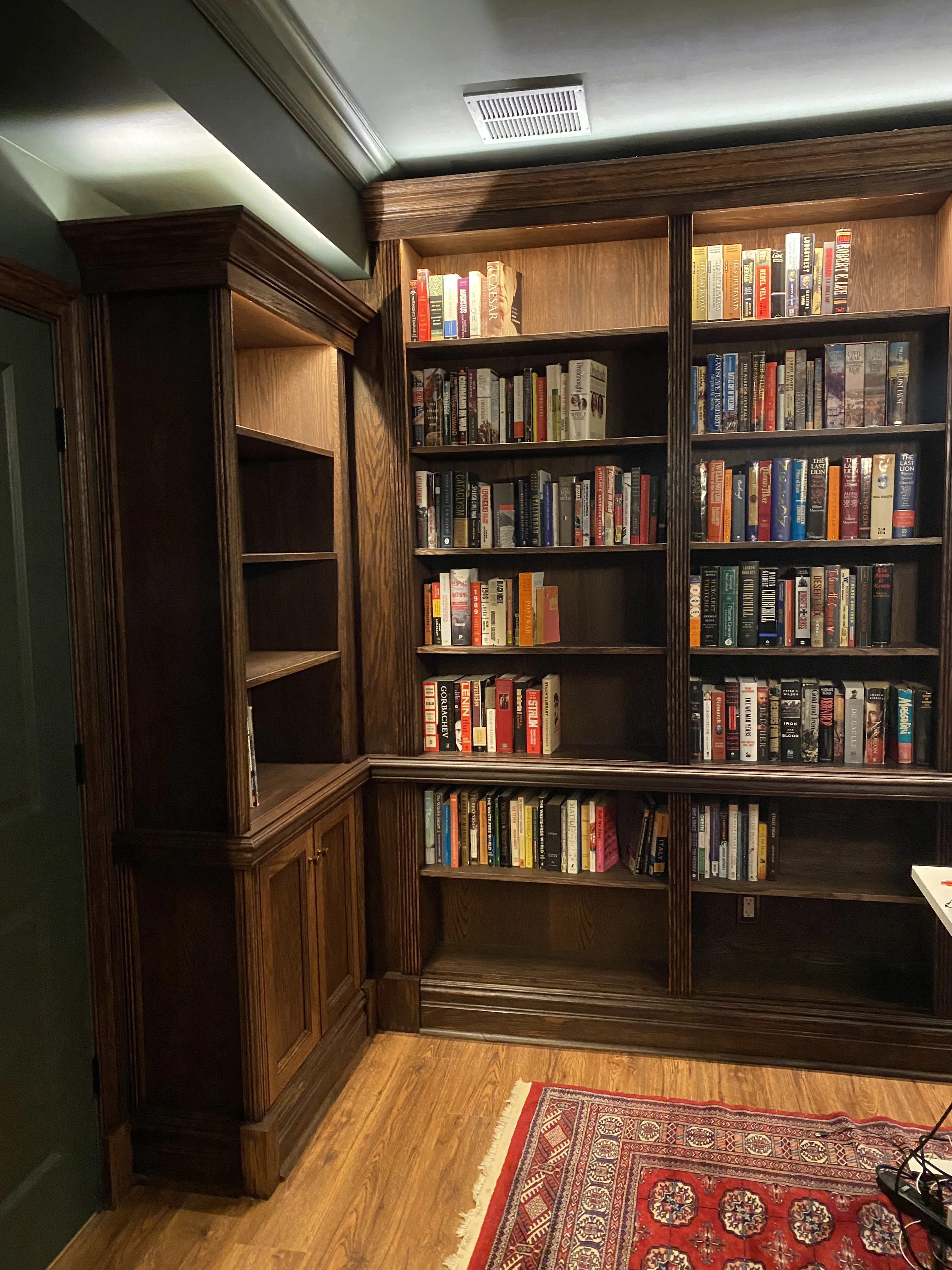 Finished custom stained-oak built-in library/study: floor-to-ceiling bookcases, base cabinets, reeded stiles, LED cove lighting