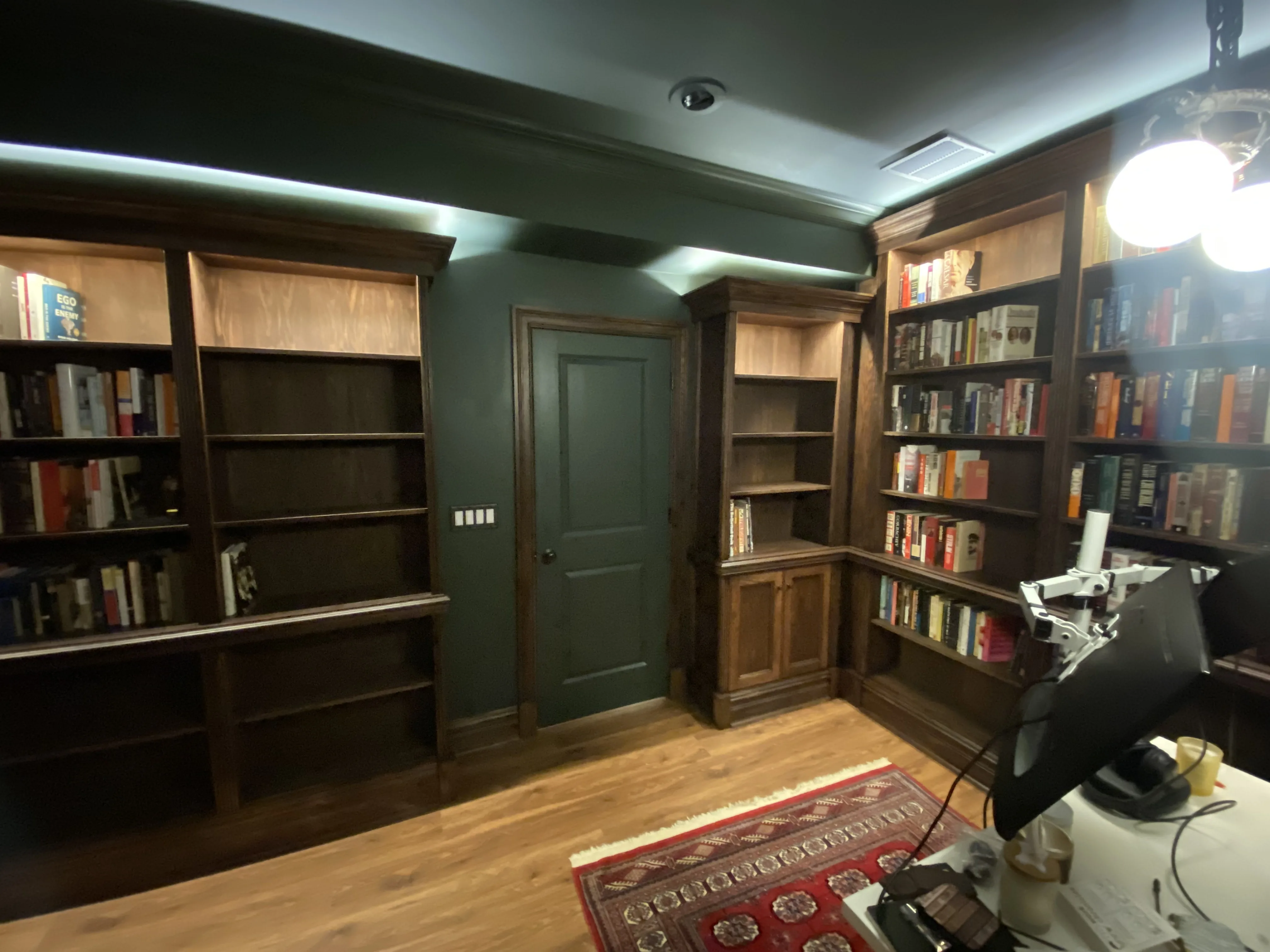 Finished custom stained-oak built-in library/study: floor-to-ceiling bookcases, base cabinets, reeded stiles, LED cove lighting