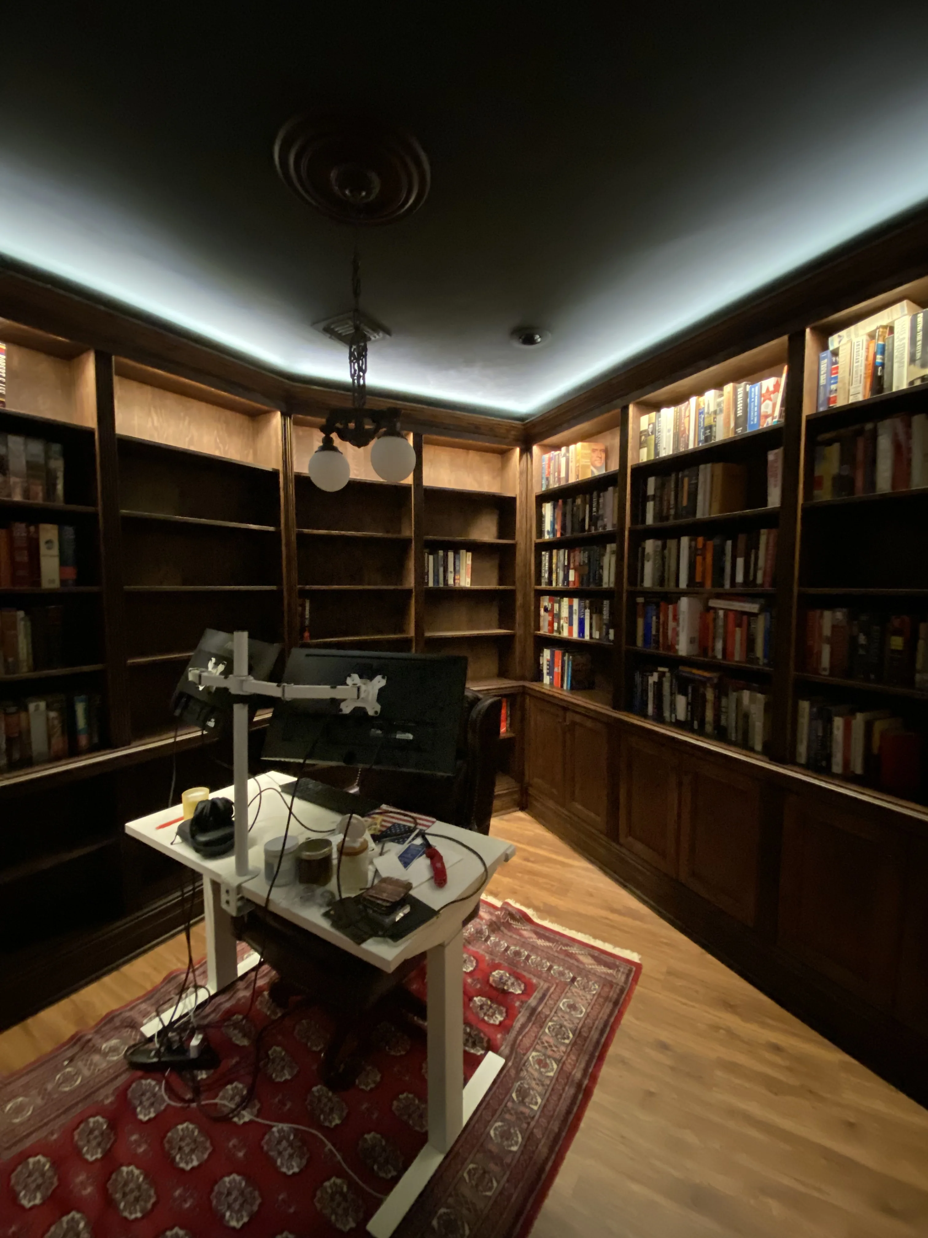 Finished custom stained-oak built-in library/study: floor-to-ceiling bookcases, base cabinets, reeded stiles, LED cove lighting