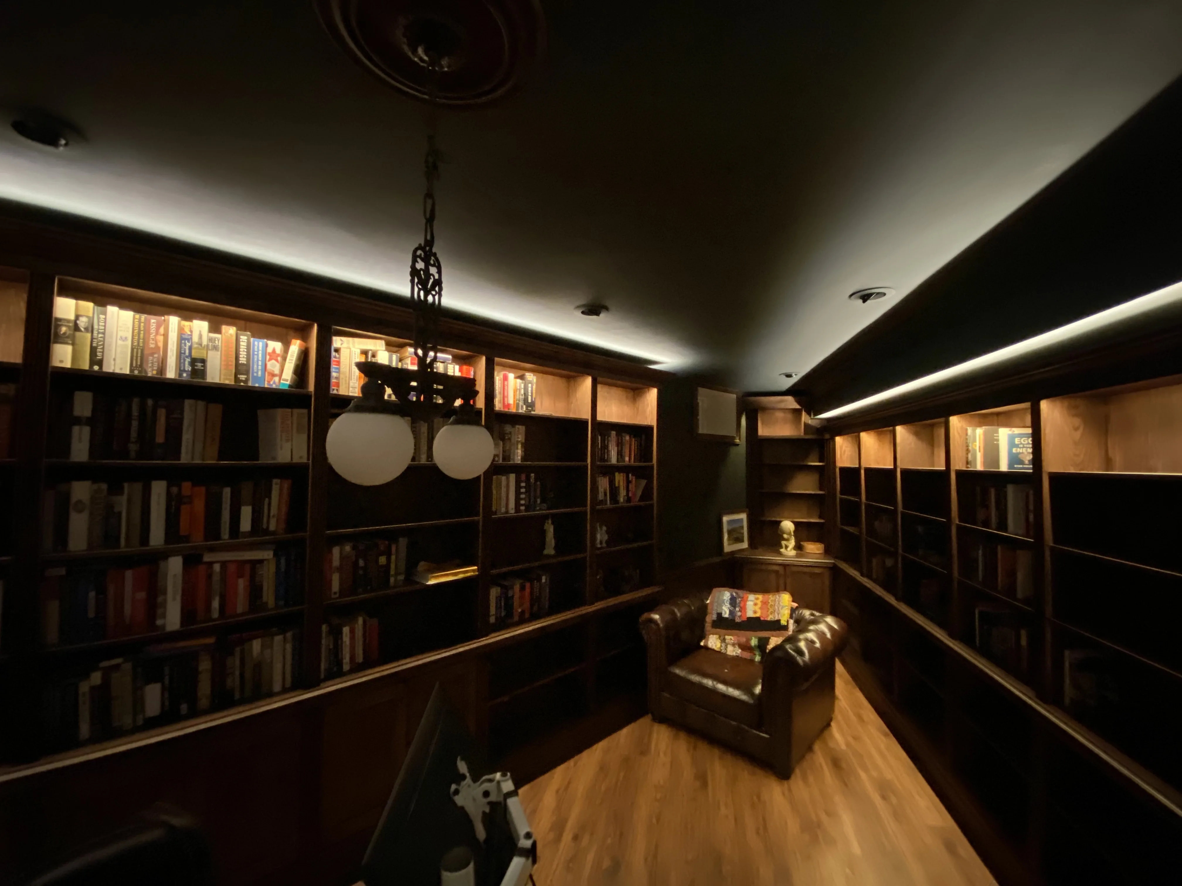 Finished custom stained-oak built-in library/study: floor-to-ceiling bookcases, base cabinets, reeded stiles, LED cove lighting