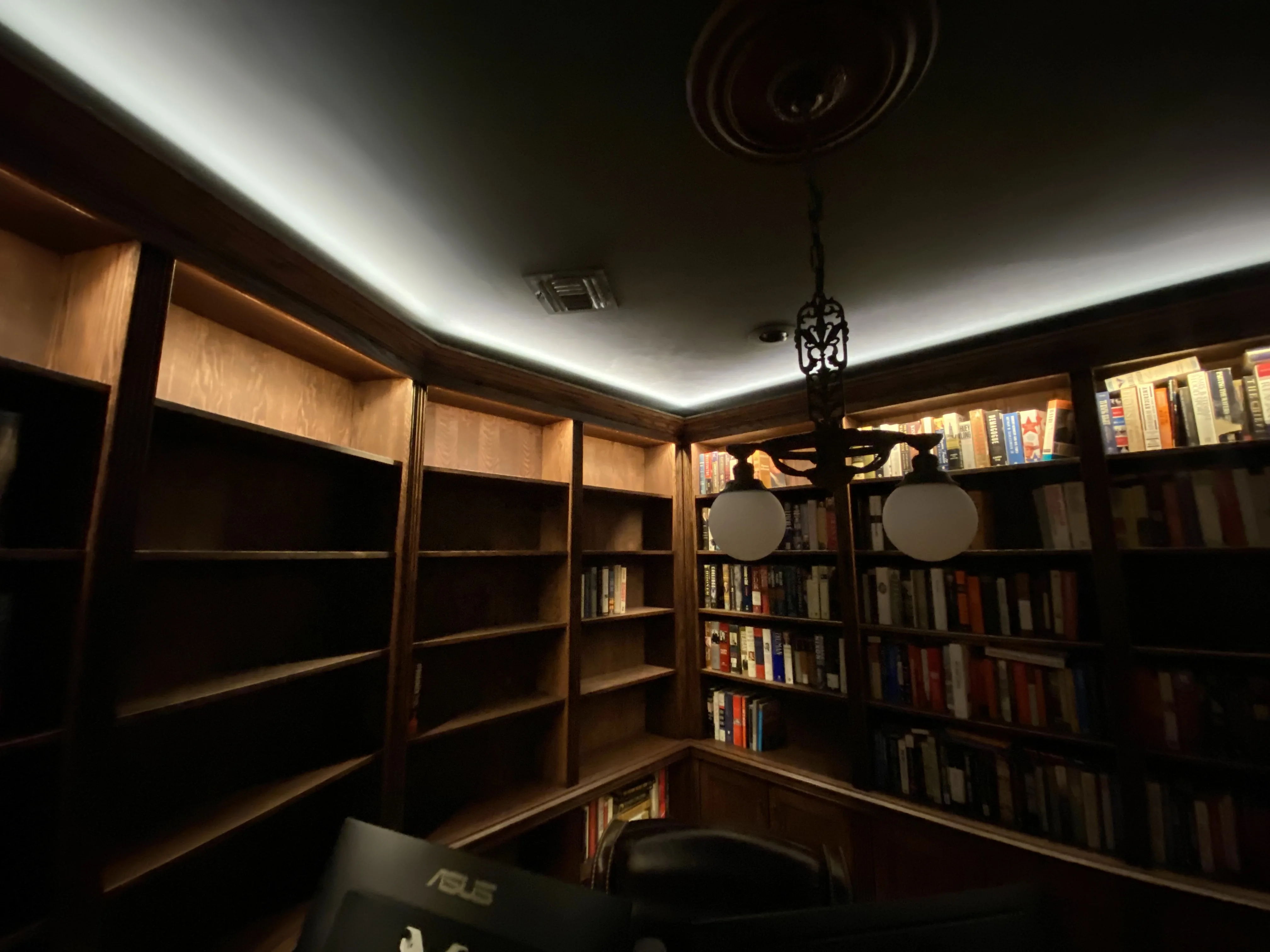 Finished custom stained-oak built-in library/study: floor-to-ceiling bookcases, base cabinets, reeded stiles, LED cove lighting