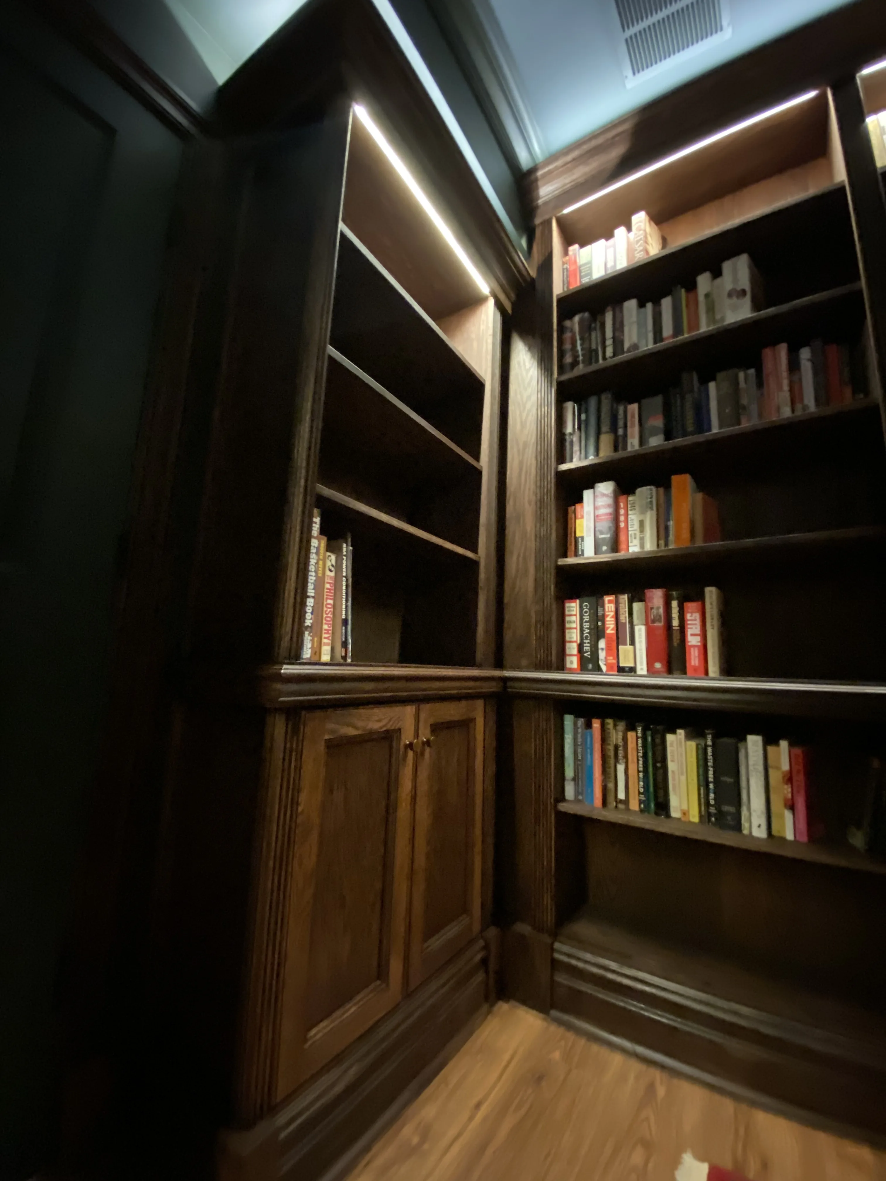 Finished custom stained-oak built-in library/study: floor-to-ceiling bookcases, base cabinets, reeded stiles, LED cove lighting