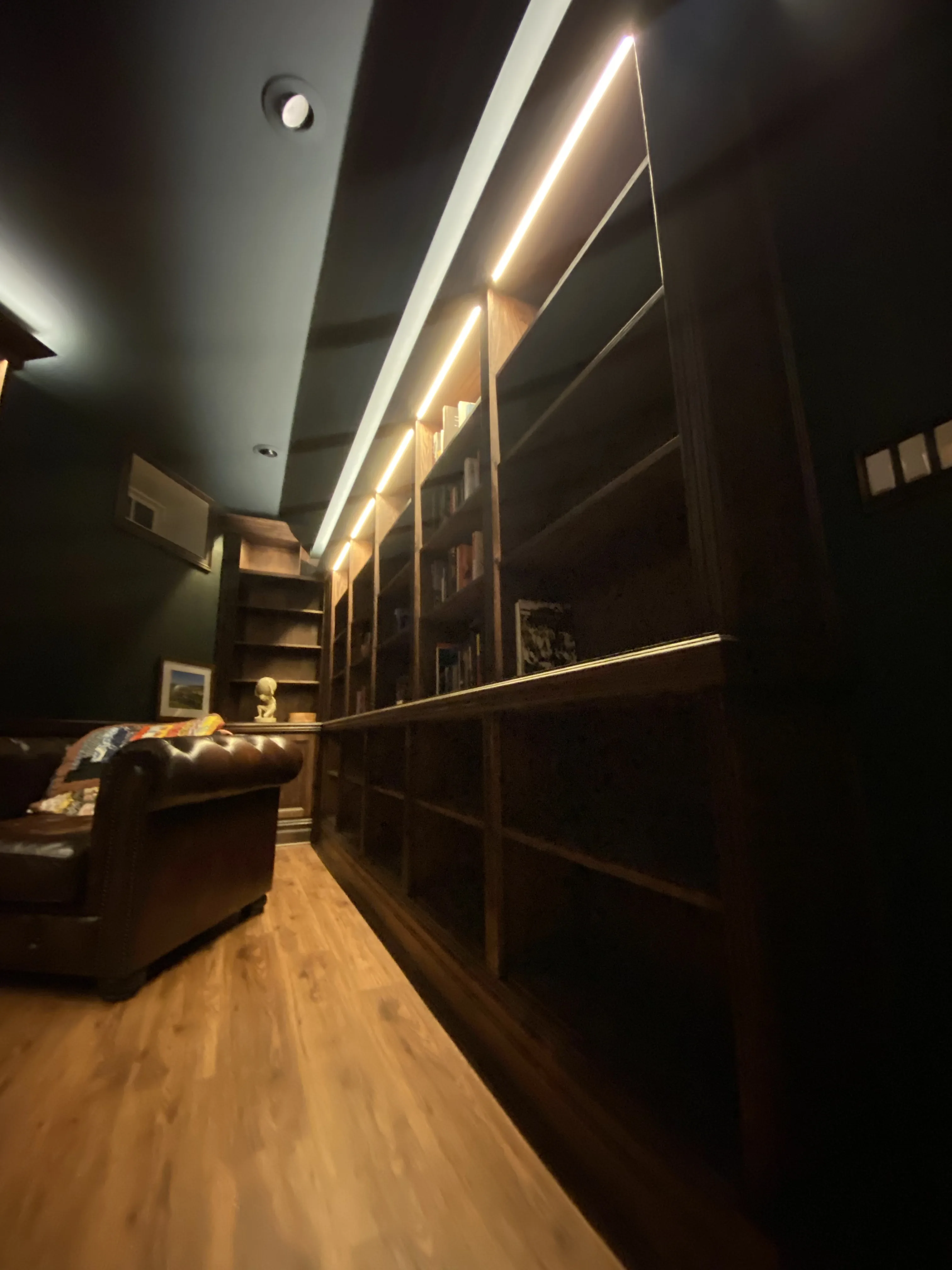 Finished custom stained-oak built-in library/study: floor-to-ceiling bookcases, base cabinets, reeded stiles, LED cove lighting