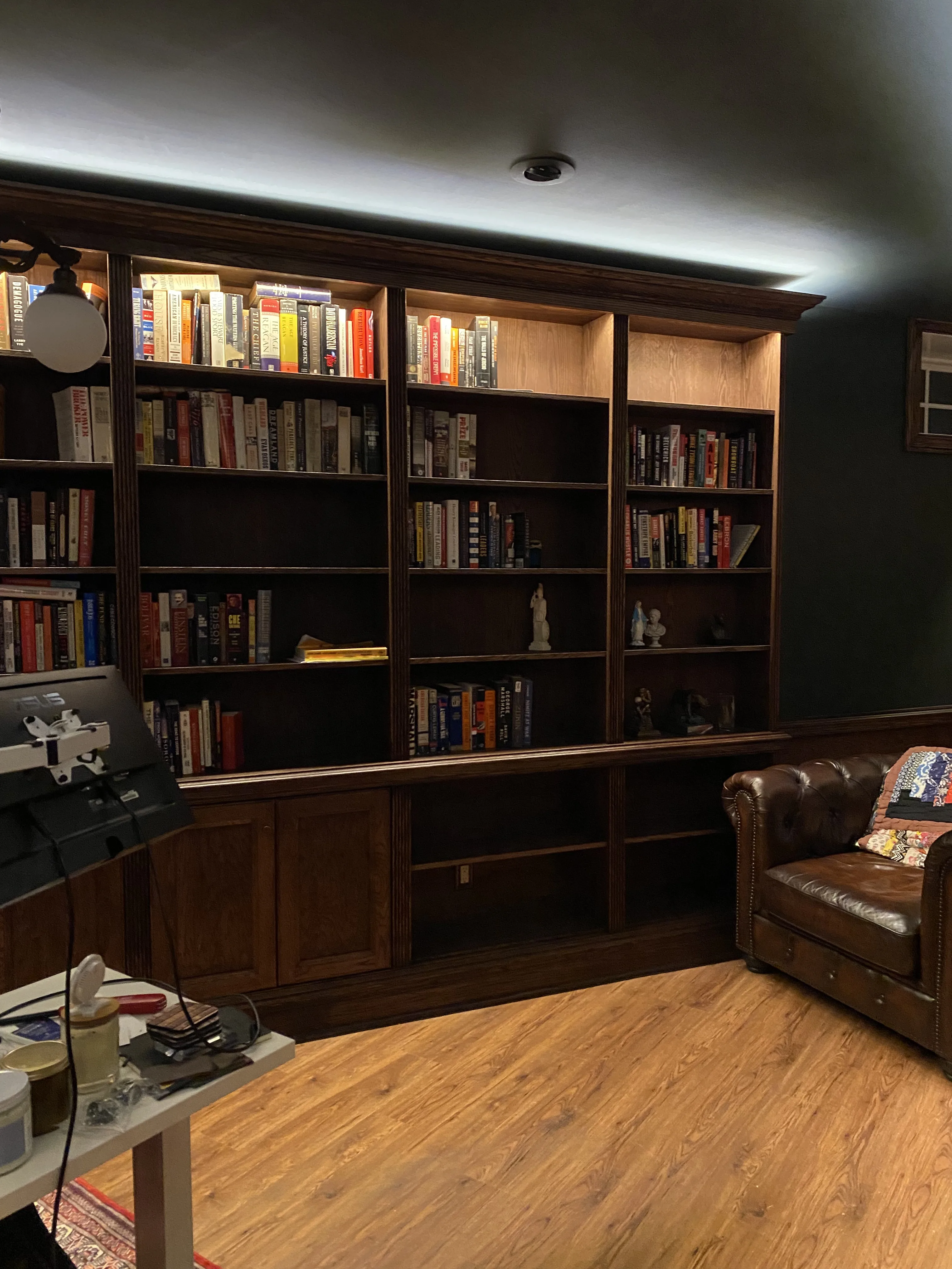 Finished custom stained-oak built-in library/study: floor-to-ceiling bookcases, base cabinets, reeded stiles, LED cove lighting