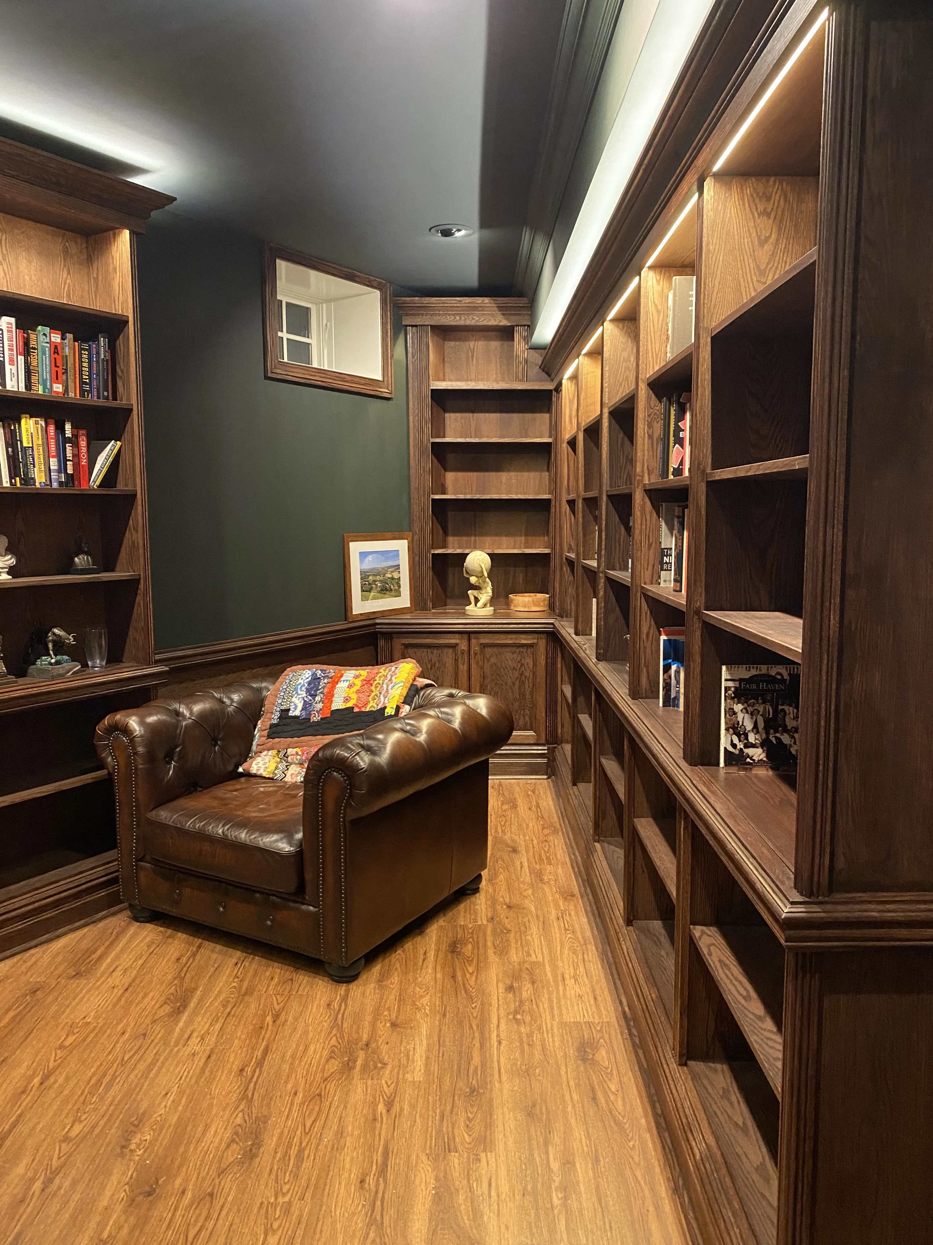 Finished custom stained-oak built-in library/study: floor-to-ceiling bookcases, base cabinets, reeded stiles, LED cove lighting