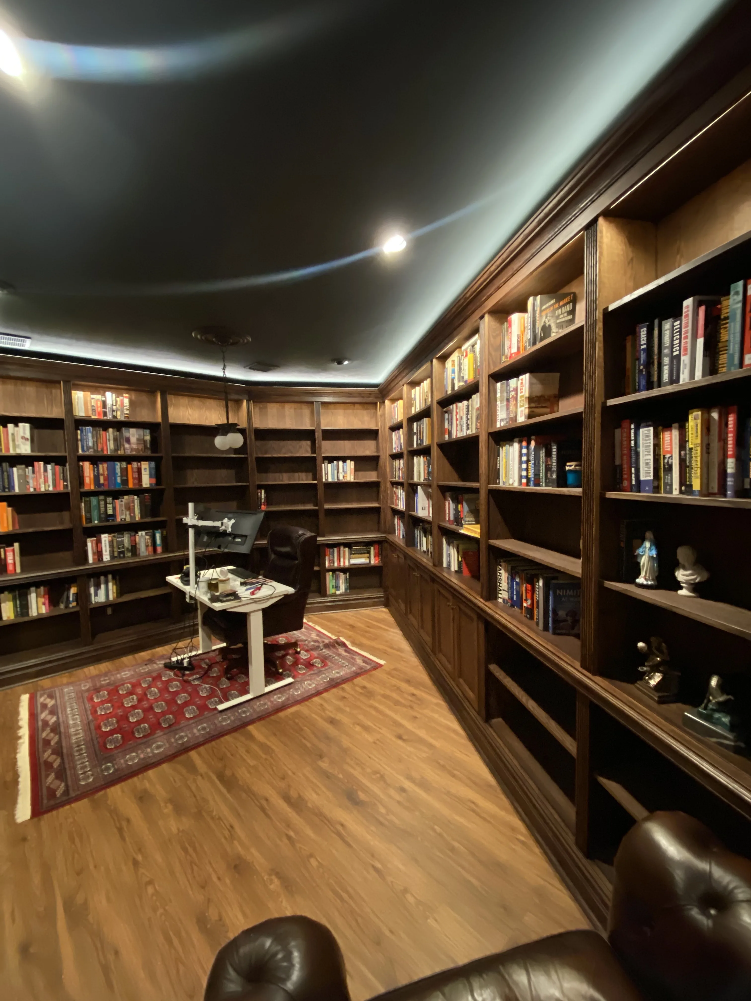 Finished custom stained-oak built-in library/study: floor-to-ceiling bookcases, base cabinets, reeded stiles, LED cove lighting