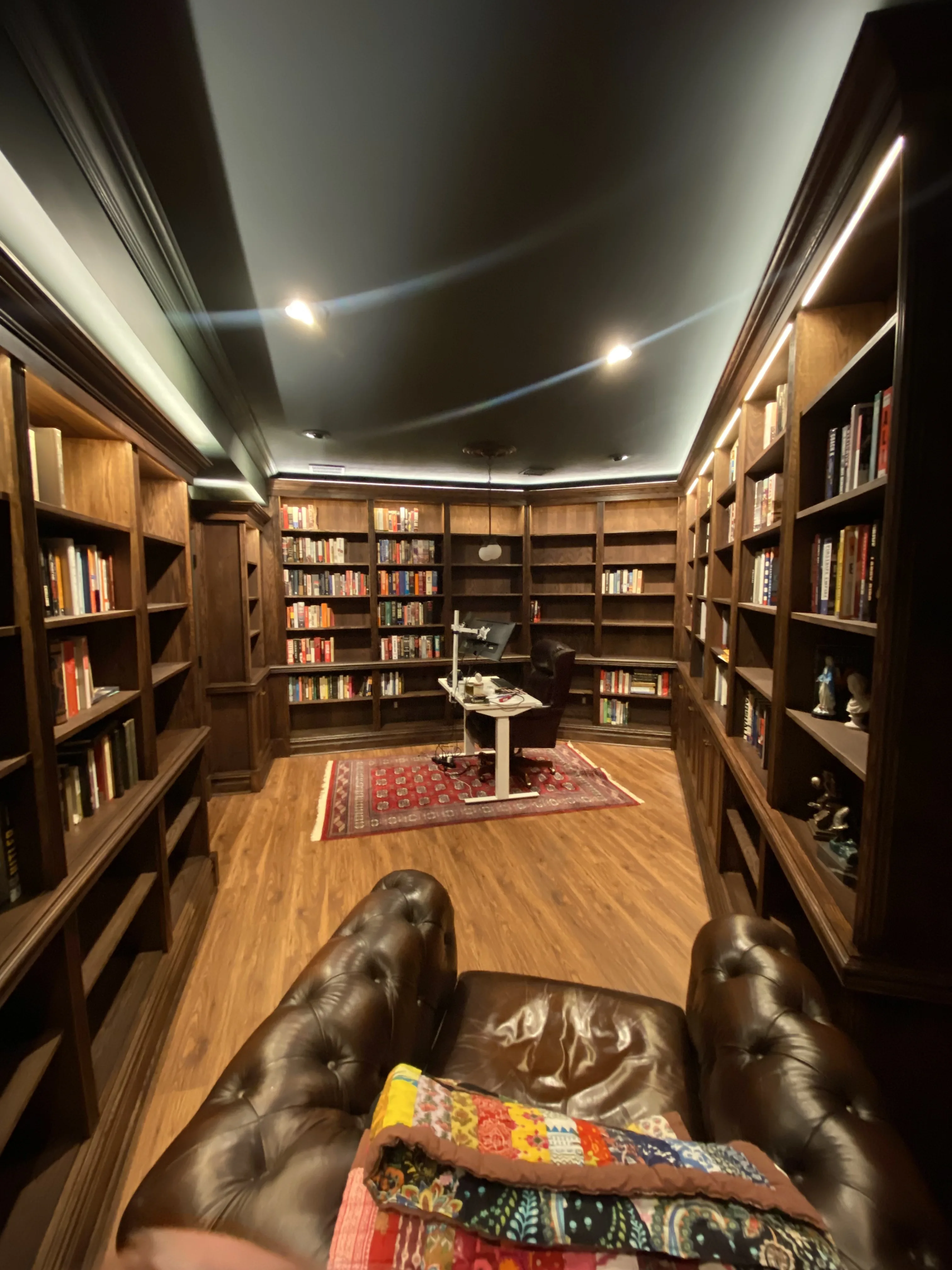 Finished custom stained-oak built-in library/study: floor-to-ceiling bookcases, base cabinets, reeded stiles, LED cove lighting