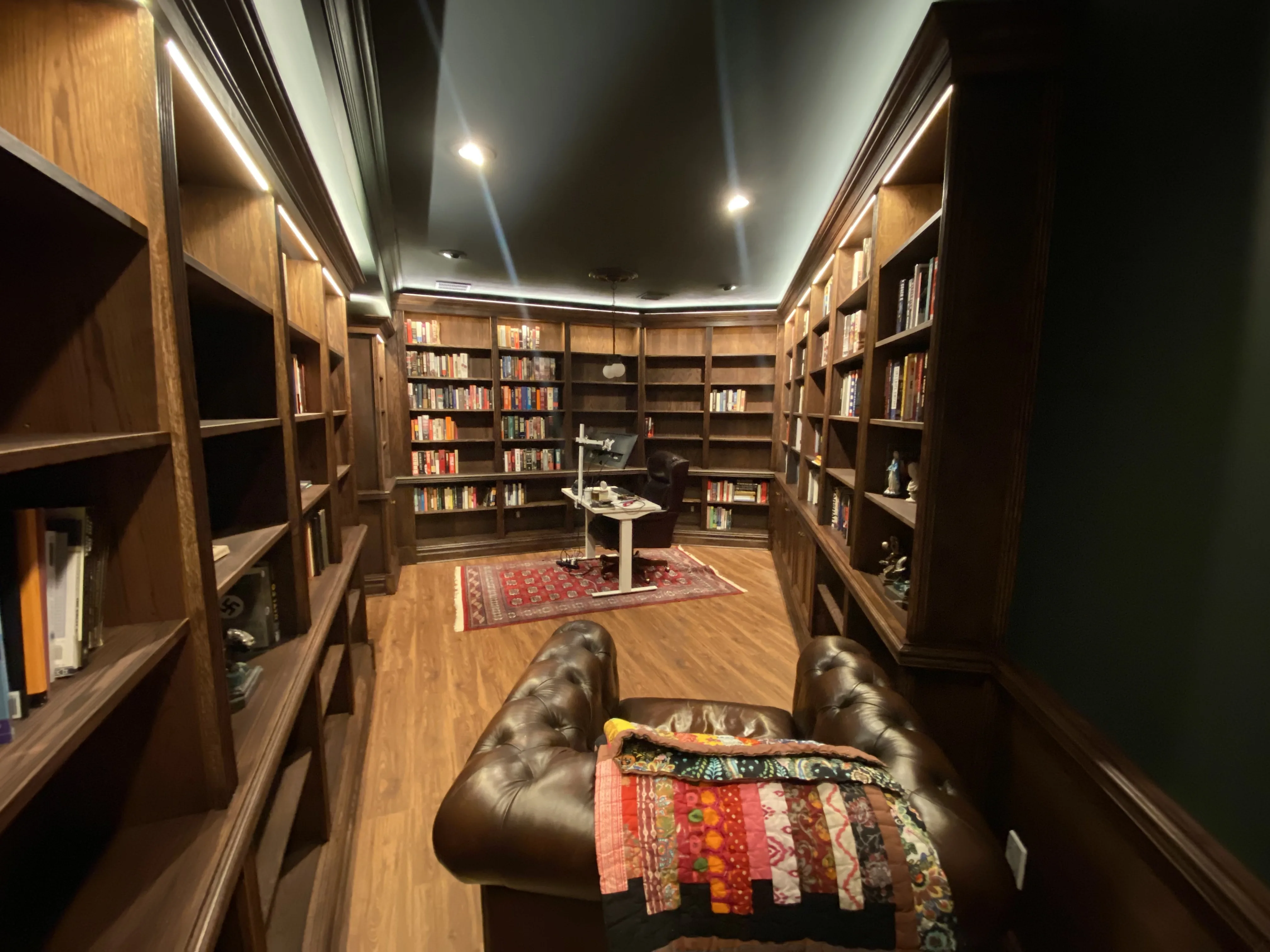 Finished custom stained-oak built-in library/study: floor-to-ceiling bookcases, base cabinets, reeded stiles, LED cove lighting