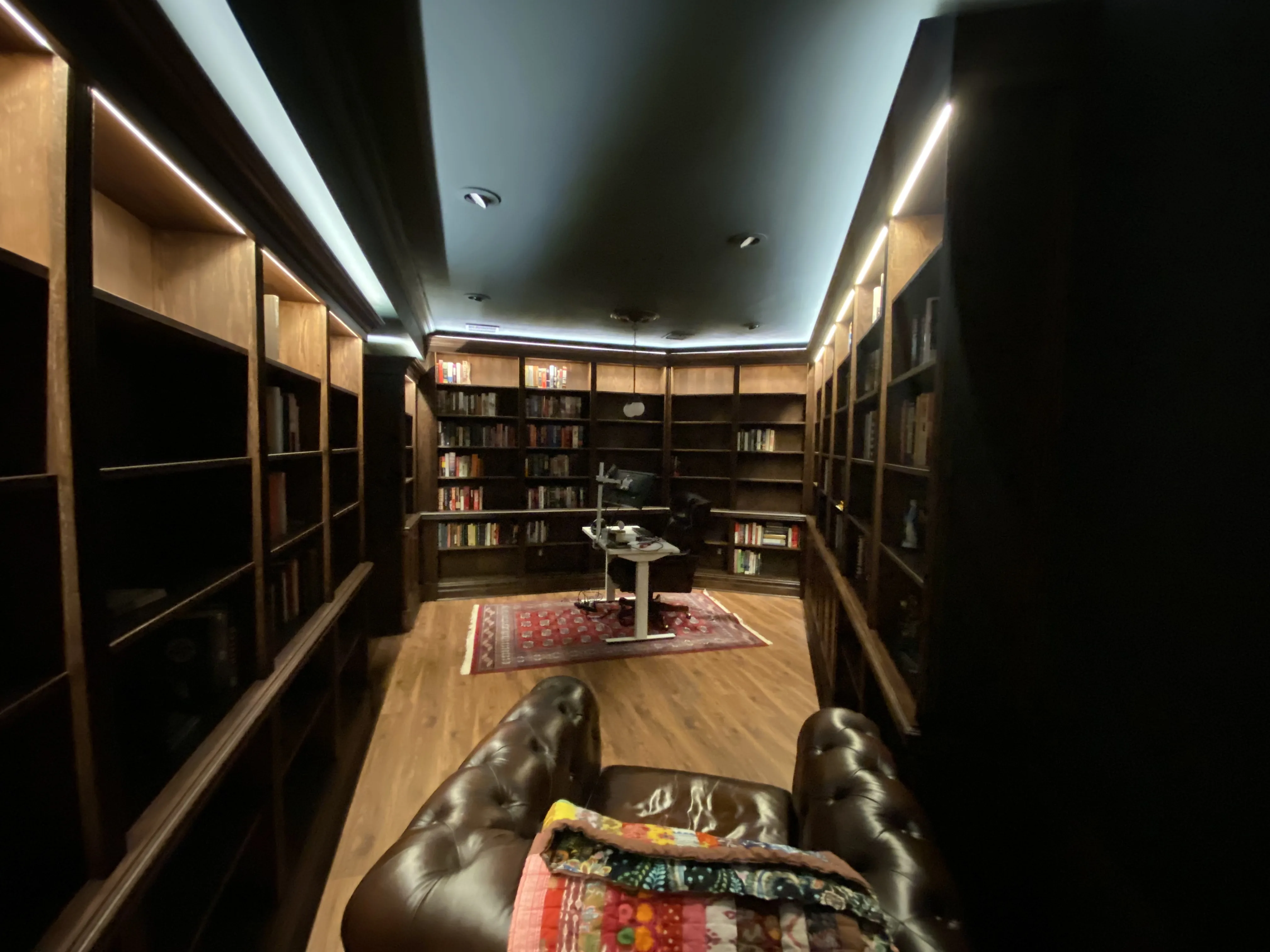 Finished custom stained-oak built-in library/study: floor-to-ceiling bookcases, base cabinets, reeded stiles, LED cove lighting
