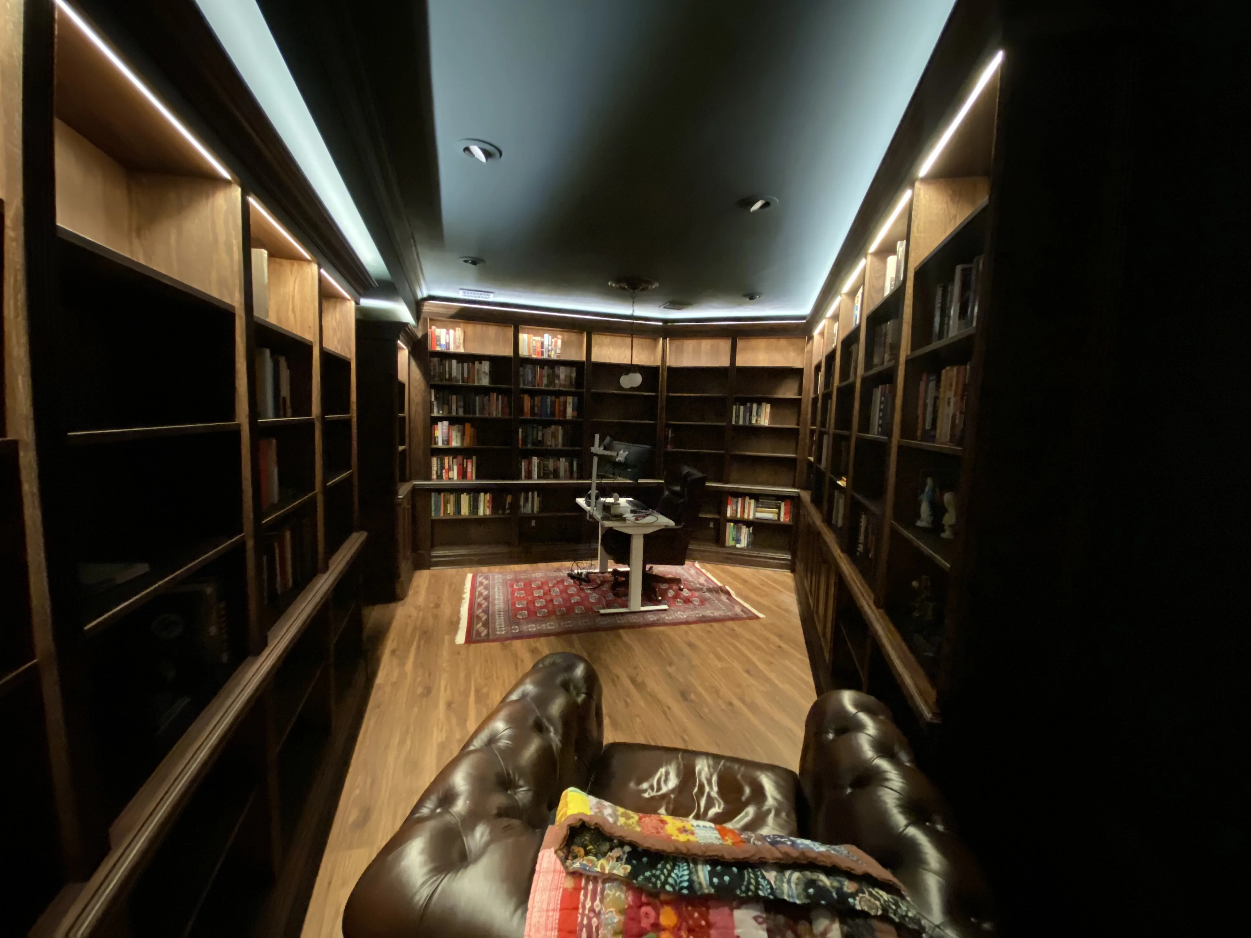 Finished custom stained-oak built-in library/study: floor-to-ceiling bookcases, base cabinets, reeded stiles, LED cove lighting