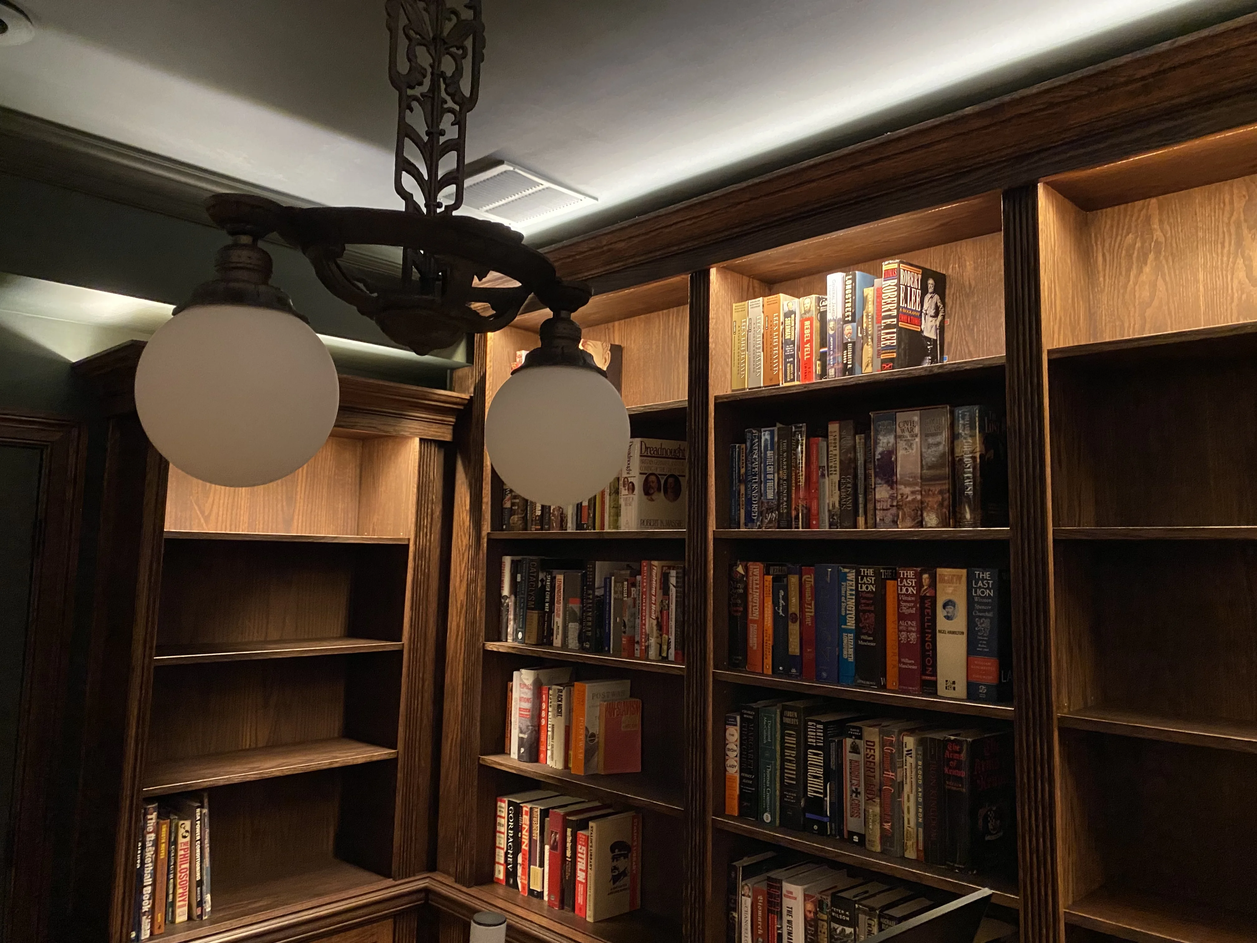 Finished custom stained-oak built-in library/study: floor-to-ceiling bookcases, base cabinets, reeded stiles, LED cove lighting