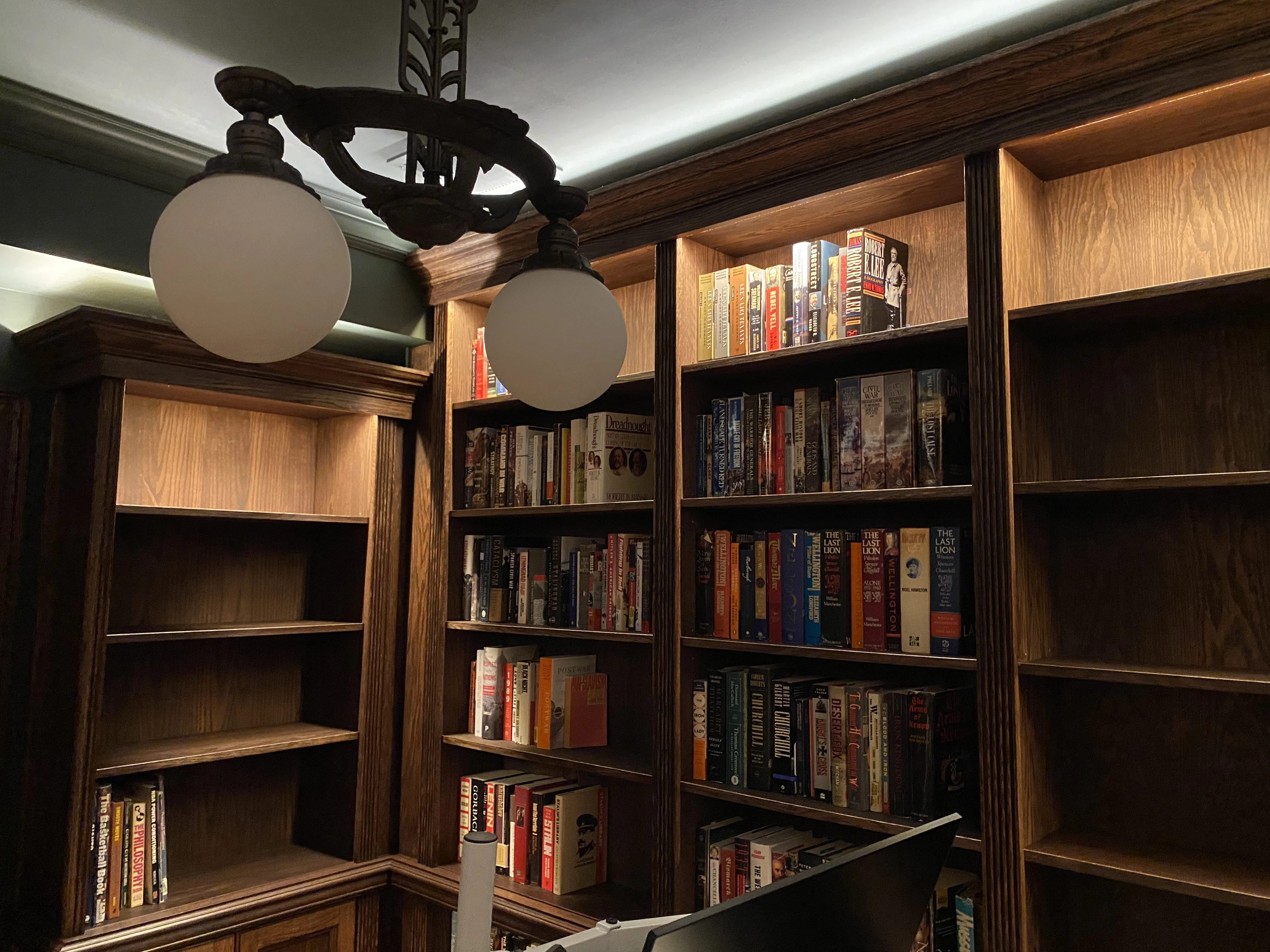 Finished custom stained-oak built-in library/study: floor-to-ceiling bookcases, base cabinets, reeded stiles, LED cove lighting
