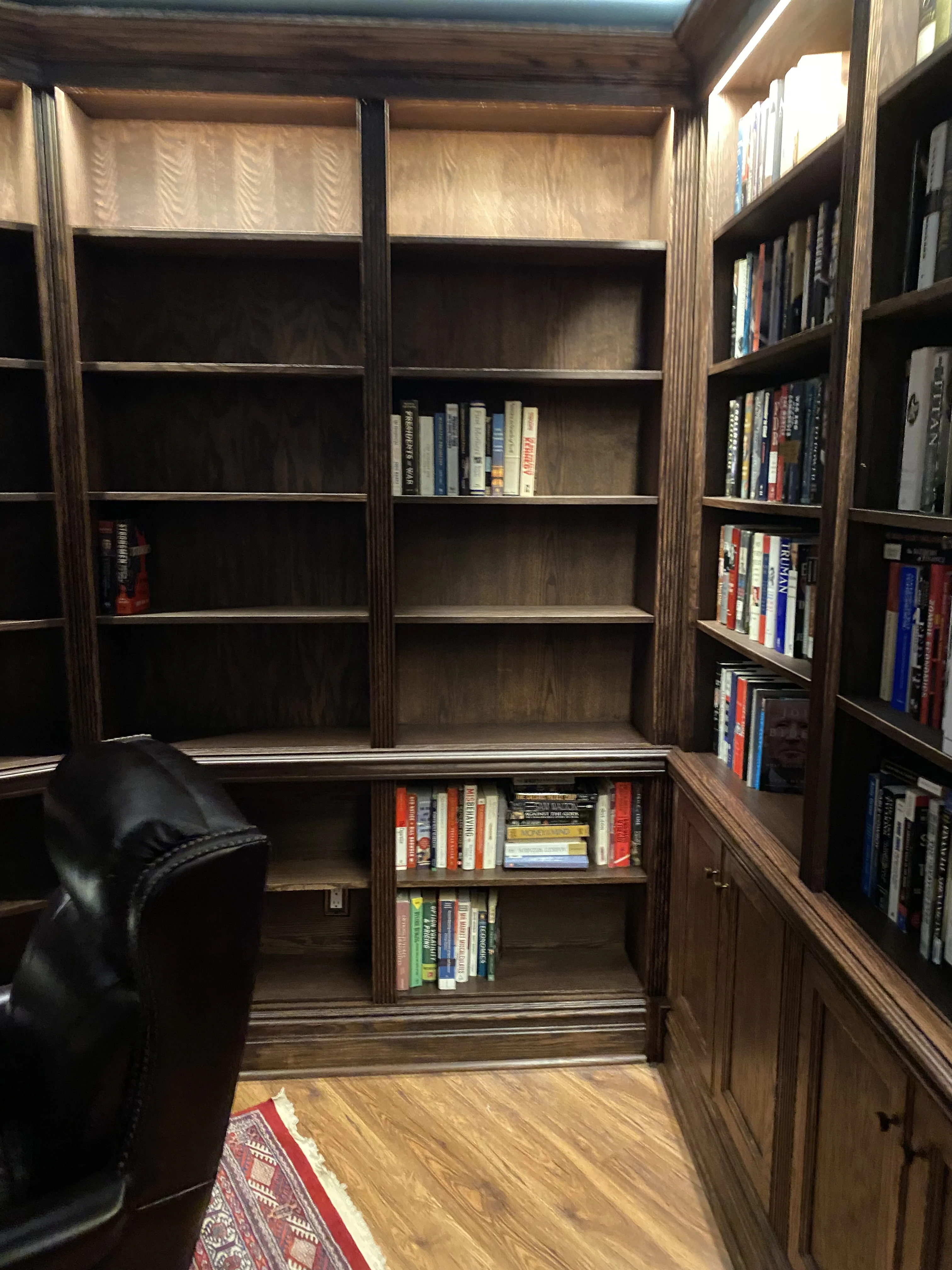 Finished custom stained-oak built-in library/study: floor-to-ceiling bookcases, base cabinets, reeded stiles, LED cove lighting