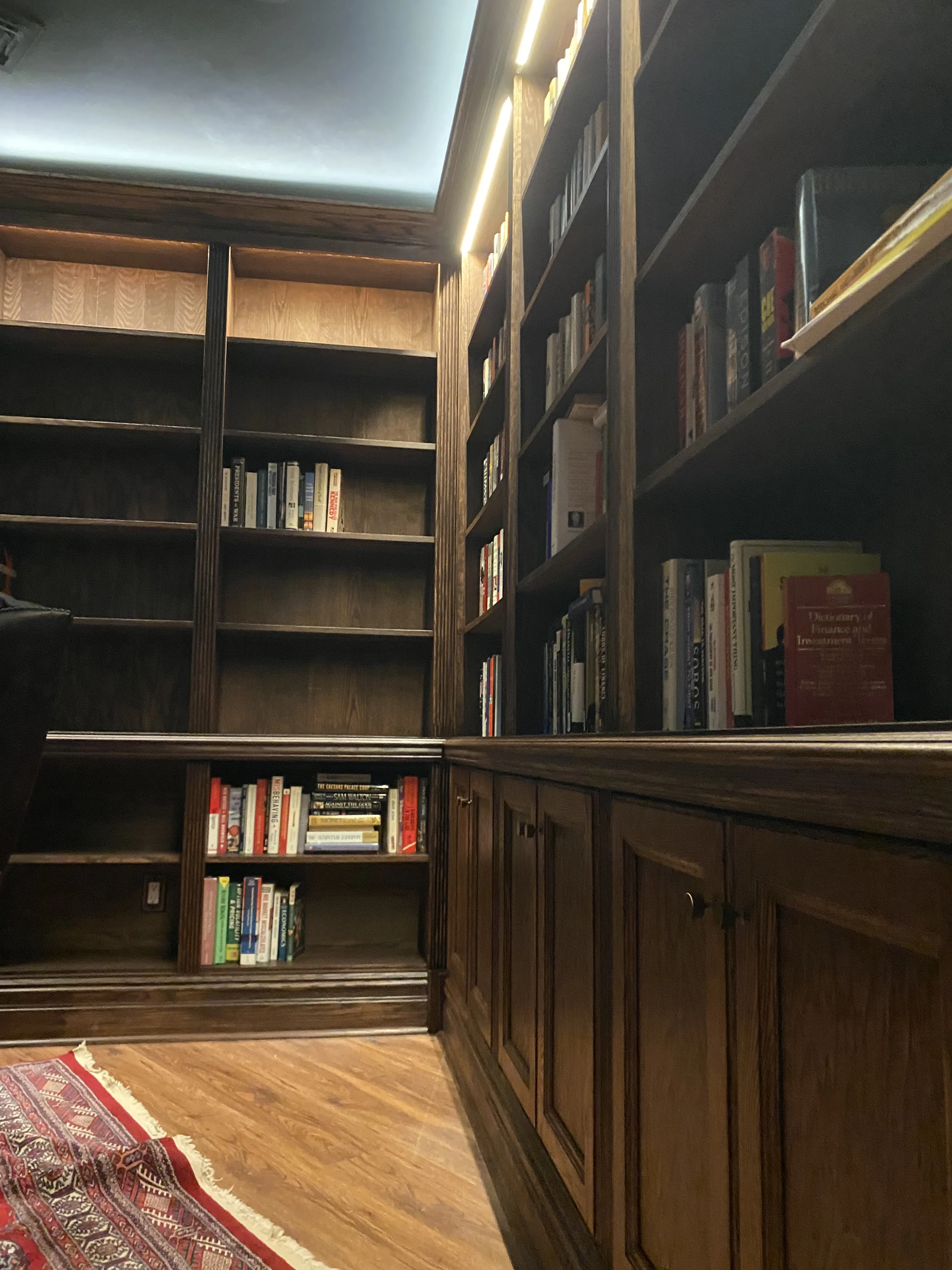 Finished custom stained-oak built-in library/study: floor-to-ceiling bookcases, base cabinets, reeded stiles, LED cove lighting