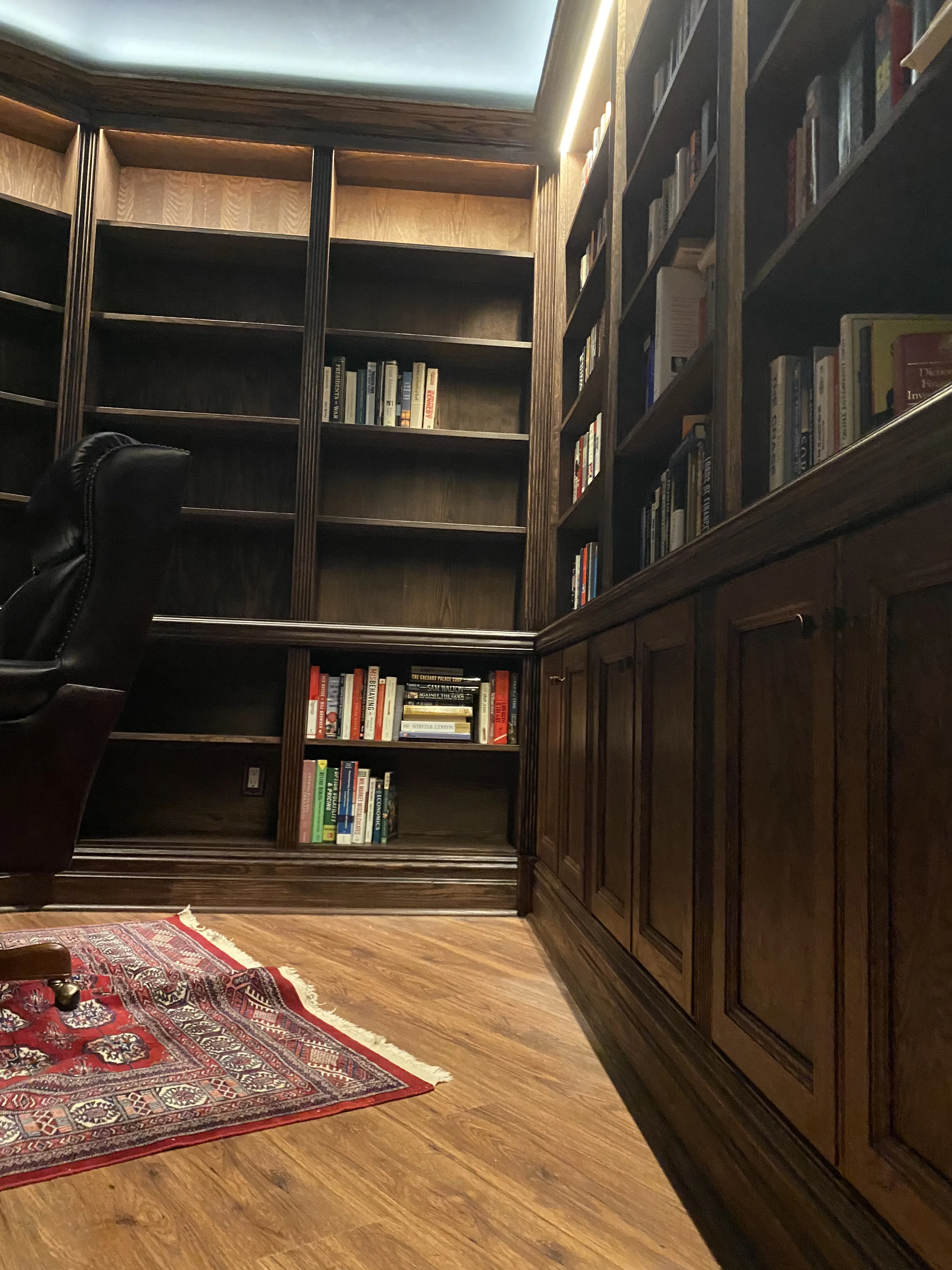 Finished custom stained-oak built-in library/study: floor-to-ceiling bookcases, base cabinets, reeded stiles, LED cove lighting