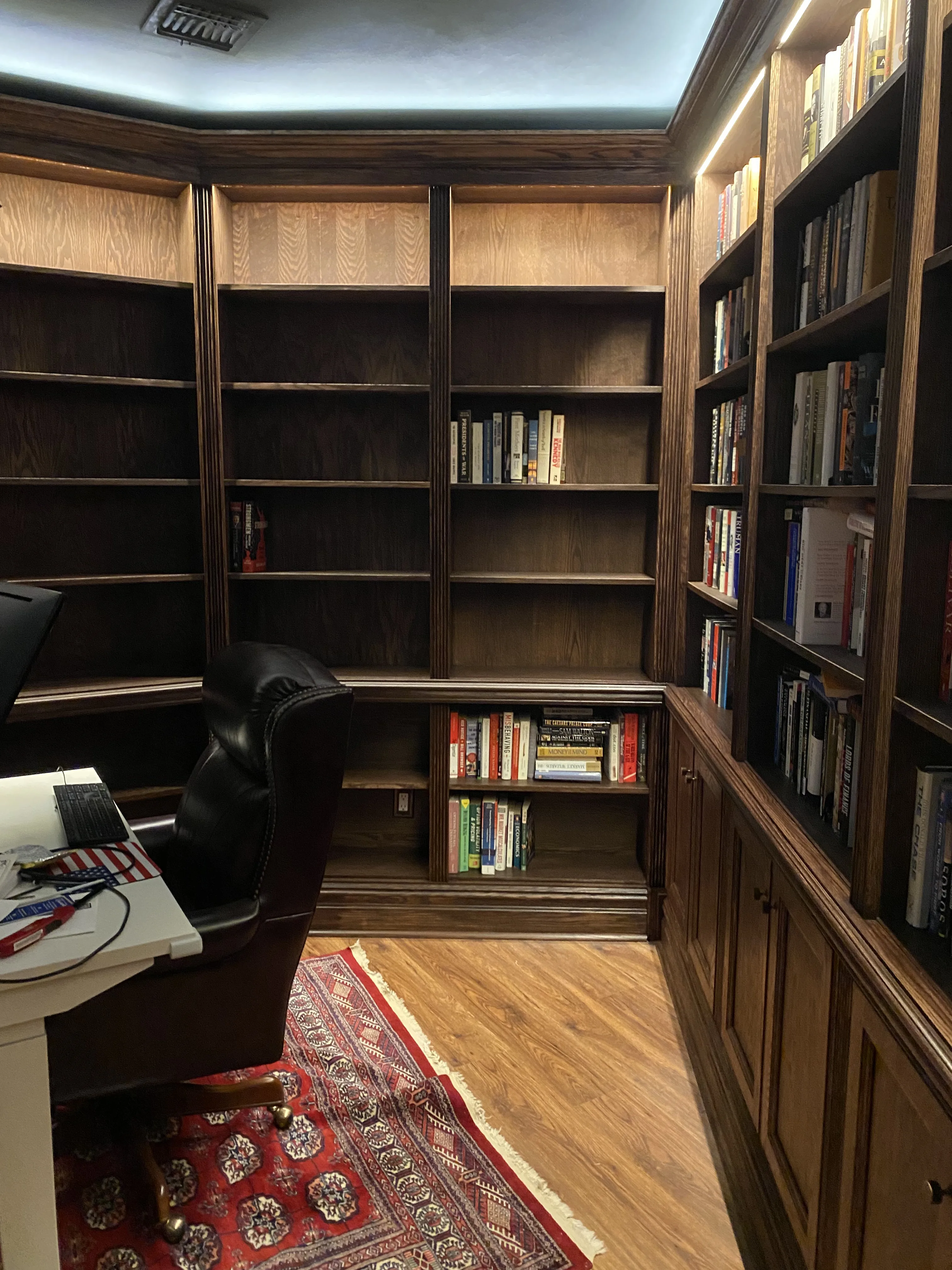 Finished custom stained-oak built-in library/study: floor-to-ceiling bookcases, base cabinets, reeded stiles, LED cove lighting