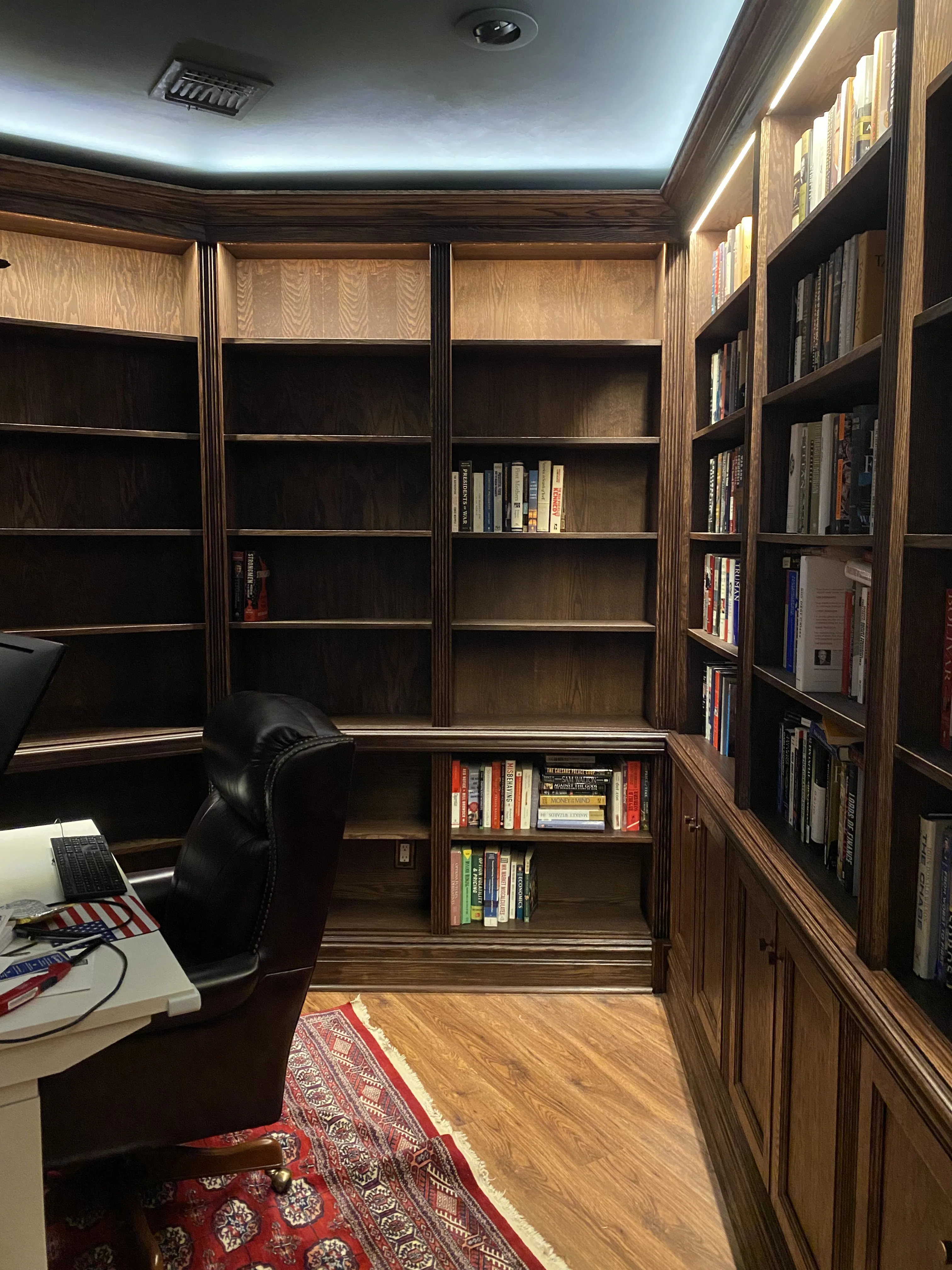 Finished custom stained-oak built-in library/study: floor-to-ceiling bookcases, base cabinets, reeded stiles, LED cove lighting